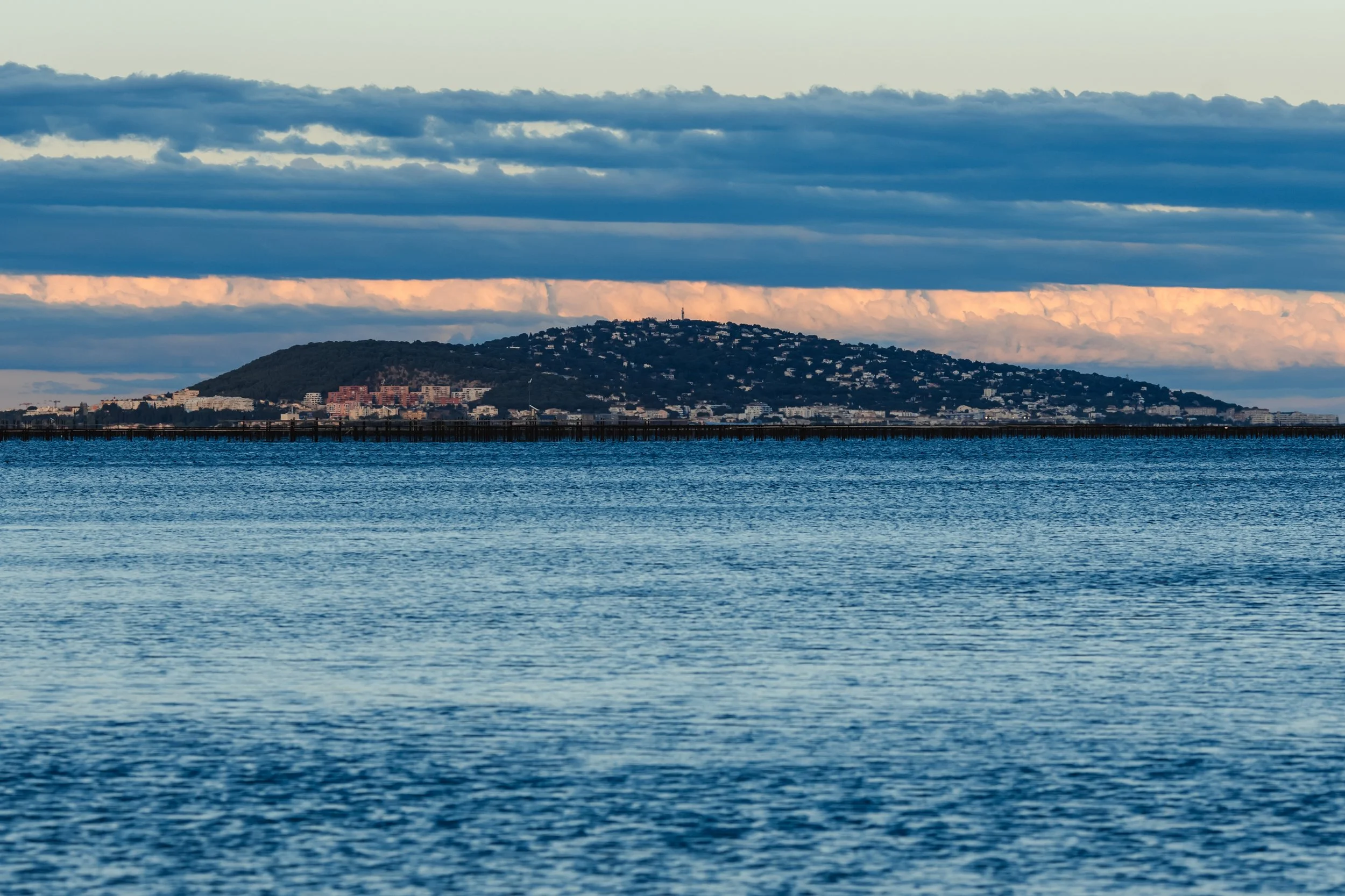 Vue d'une île avec une ville en contrebas, vue depuis la mer, avec un ciel nuageux en arrière-plan.