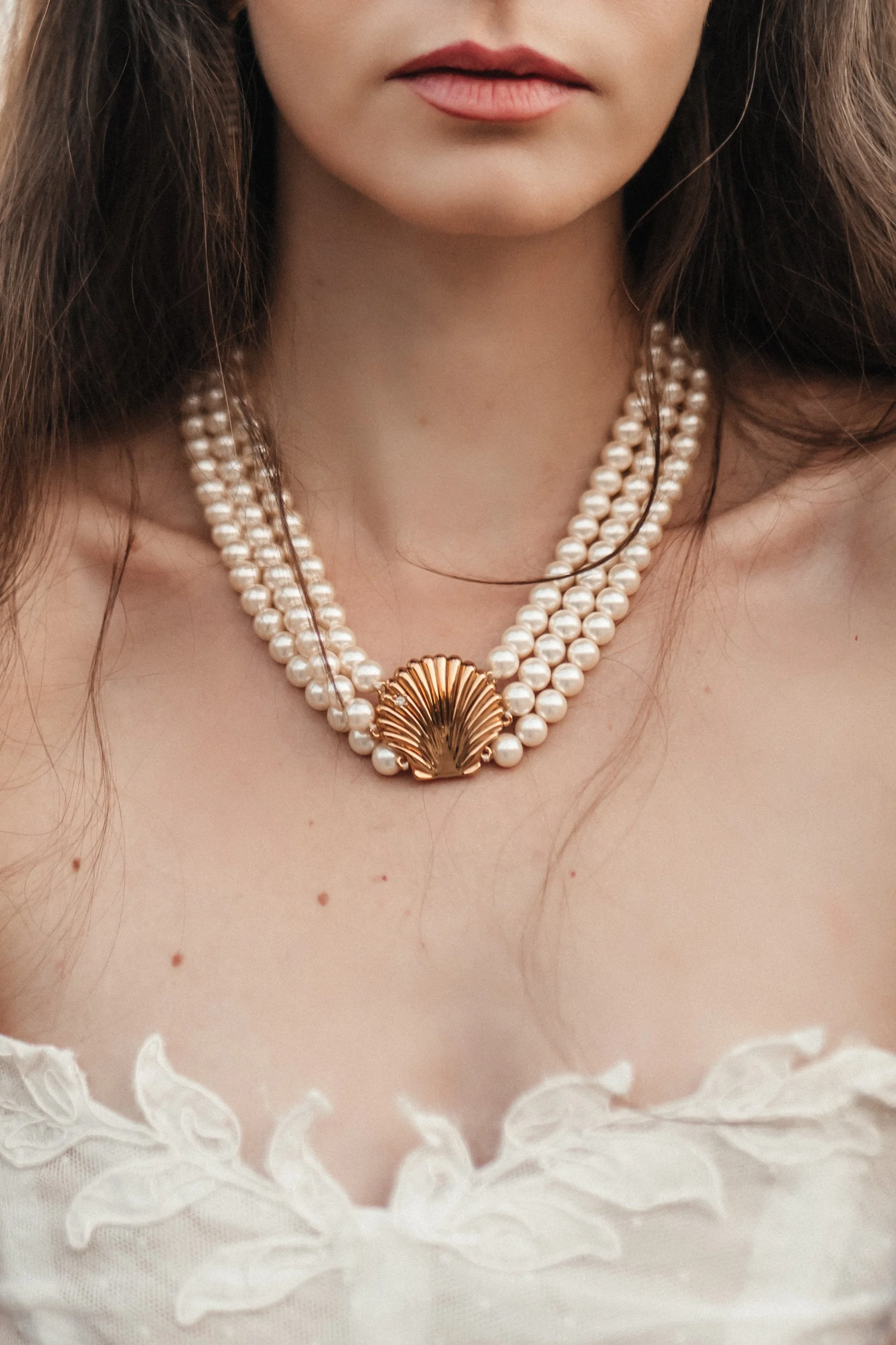 Très proche du cou d'une femme portant un collier de perles avec un pendentif en forme de coquillage doré.