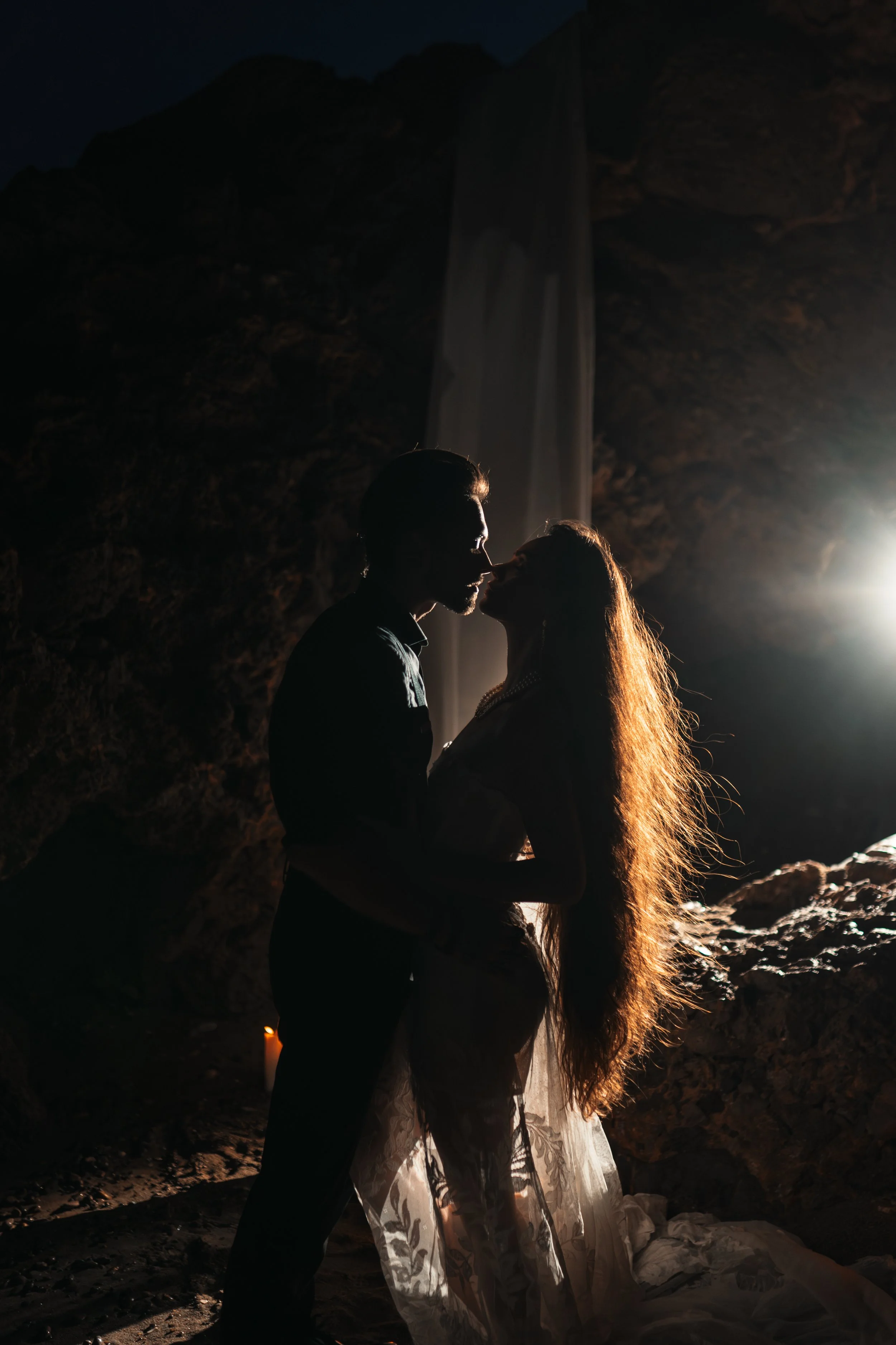 Un couple s'embrasse dans une scène romantique avec un arrière-plan de cascade au coucher du soleil.