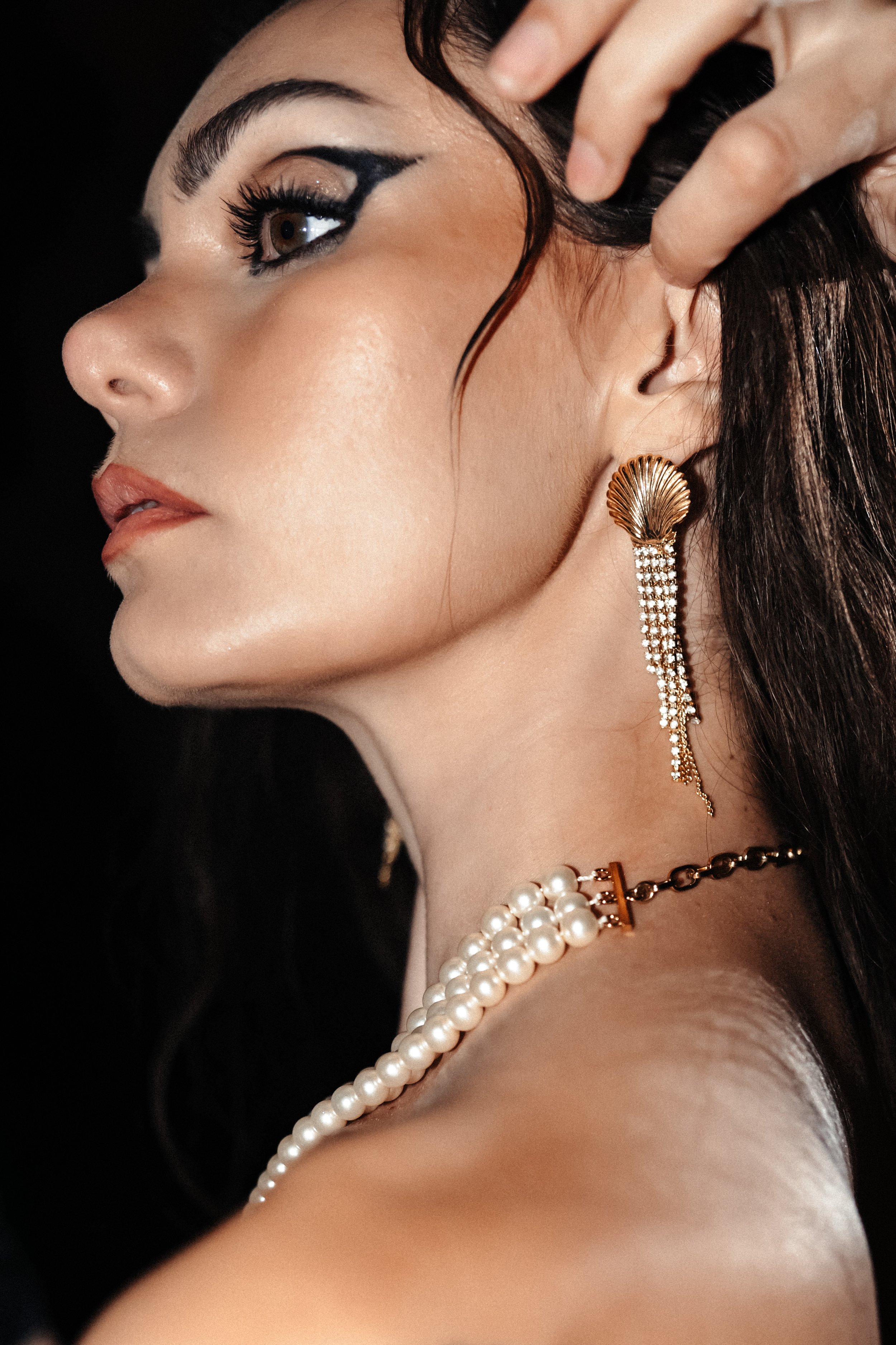 Une femme avec des boucles d'oreilles longues en dôme doré et perles, portant un collier de perles, avec maquillage élégant et cheveux foncés, portrait en gros plan