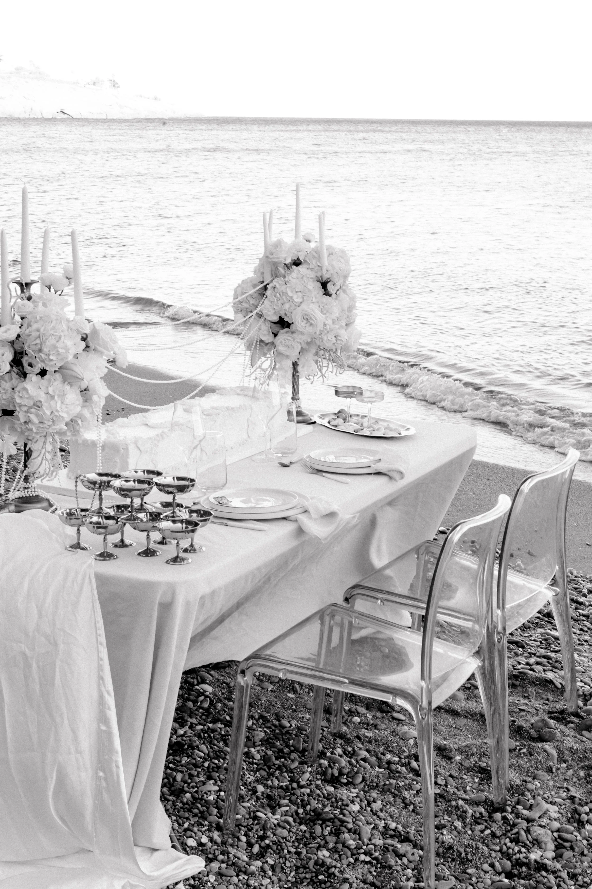 Table de mariage avec décoration florale et bougies, située sur une plage au bord de la mer.