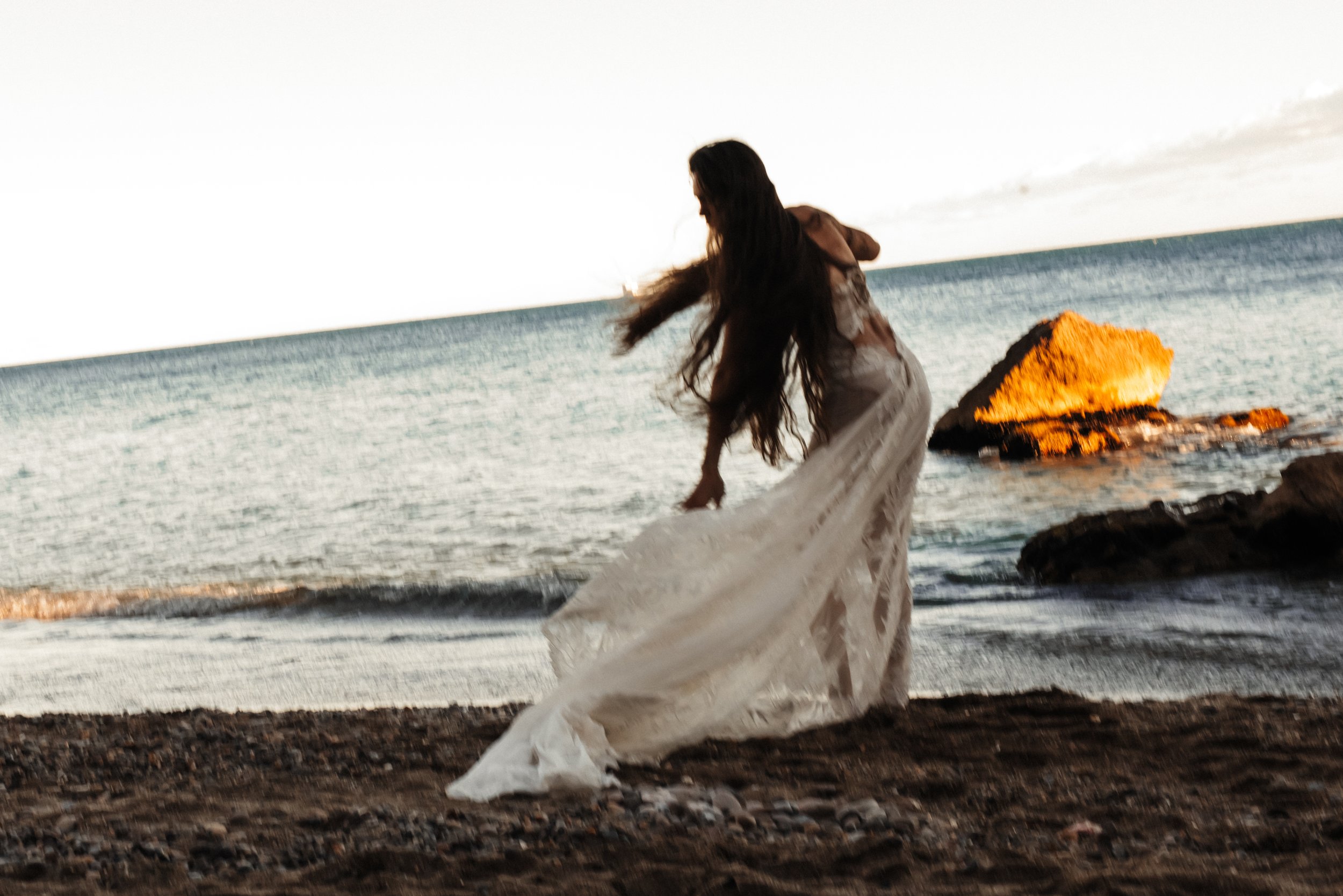 Femme en robe blanche sur la plage au coucher du soleil.