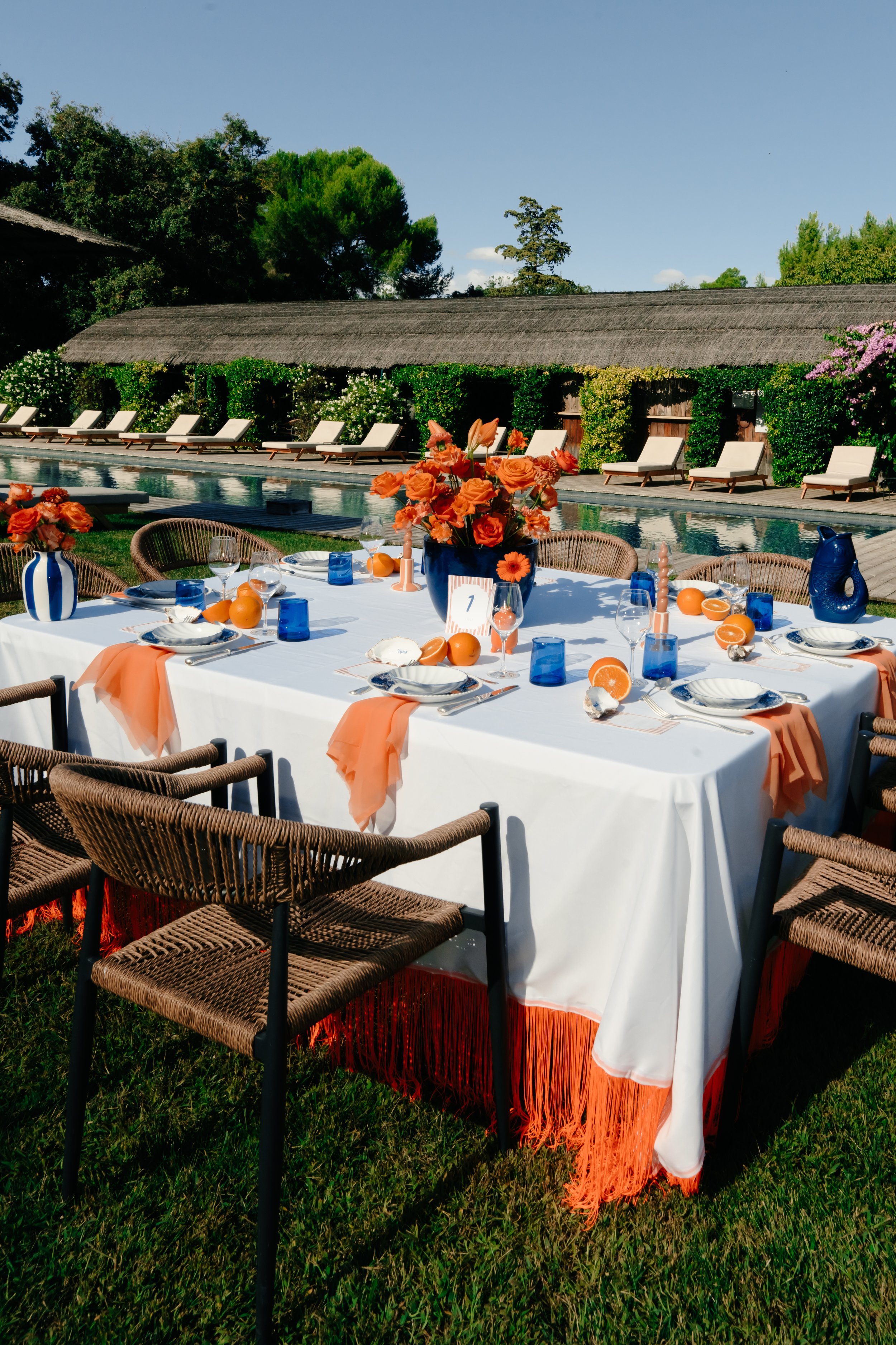 Table de dîner décorée avec des fleurs orange, des fruits et des verres, en extérieur près d'une piscine
