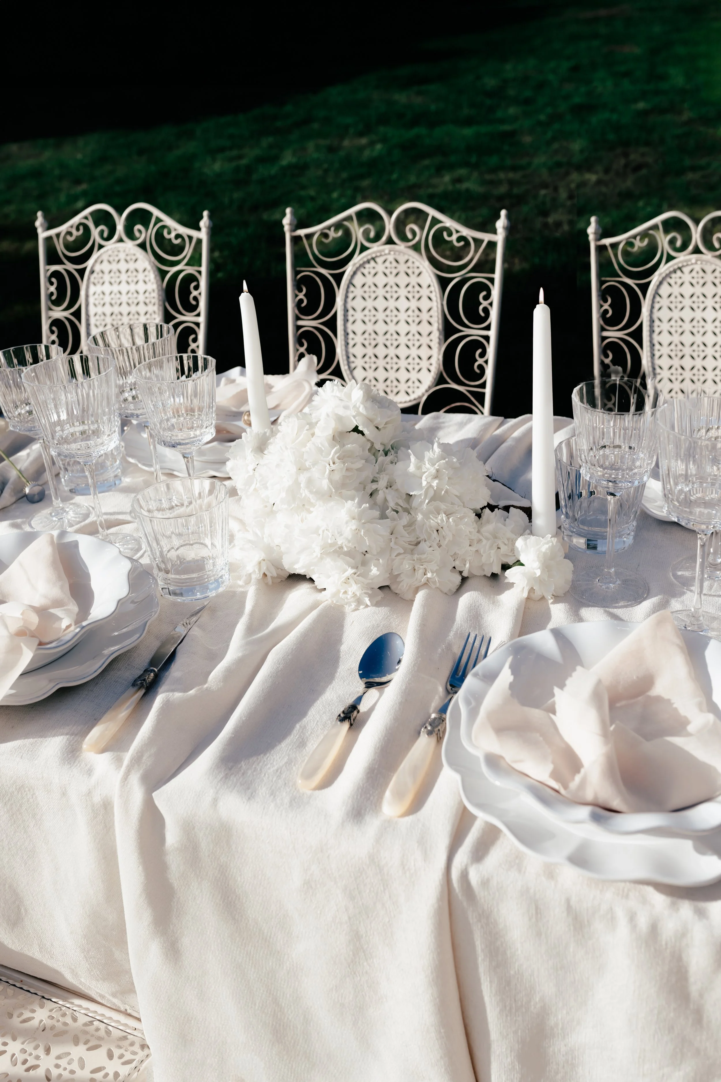 Une femme en robe de mariée blanche devant une table dressée pour un dîner, près d'une piscine.