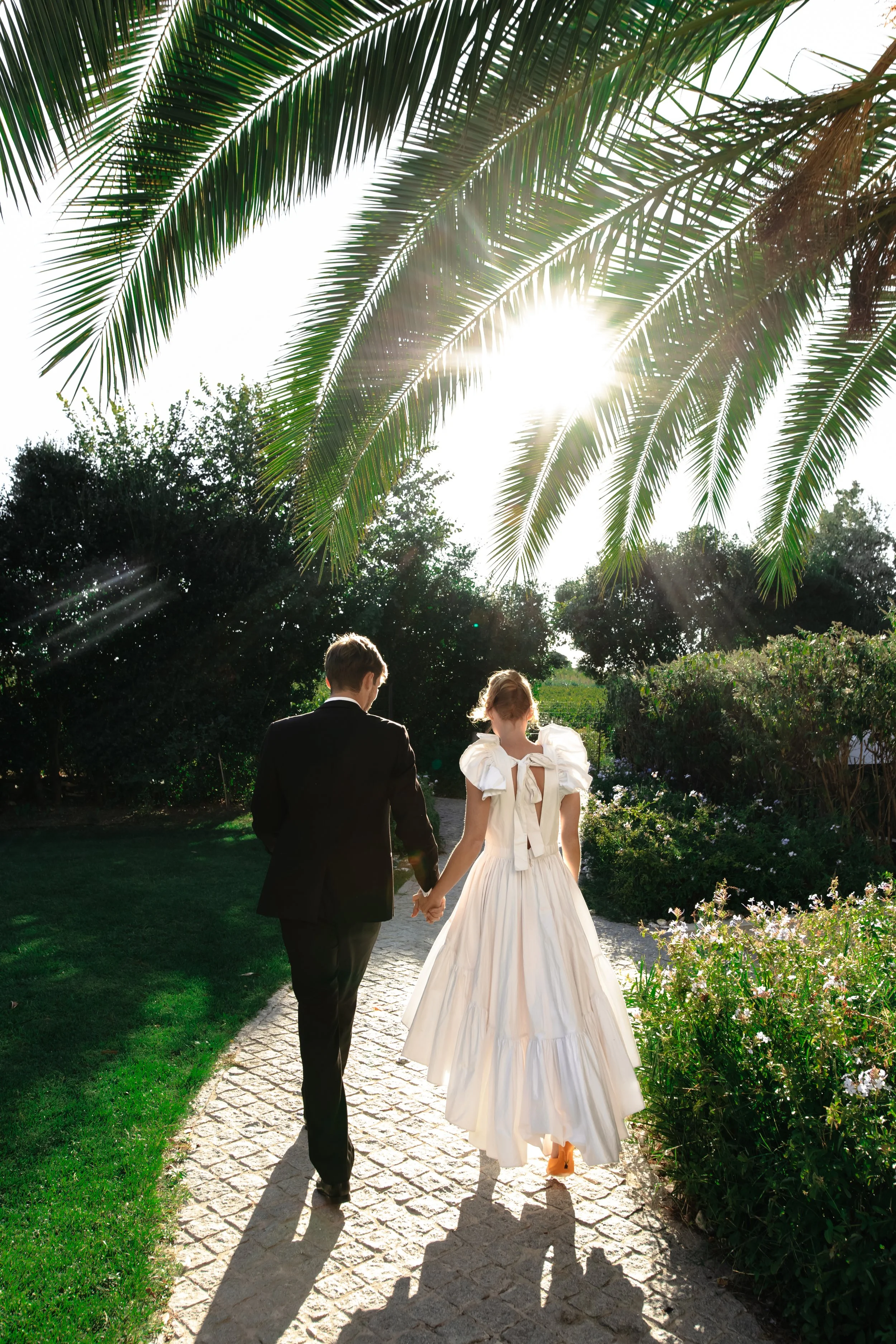 un couple habillé en mariage marche sous un palmier dans un jardin
