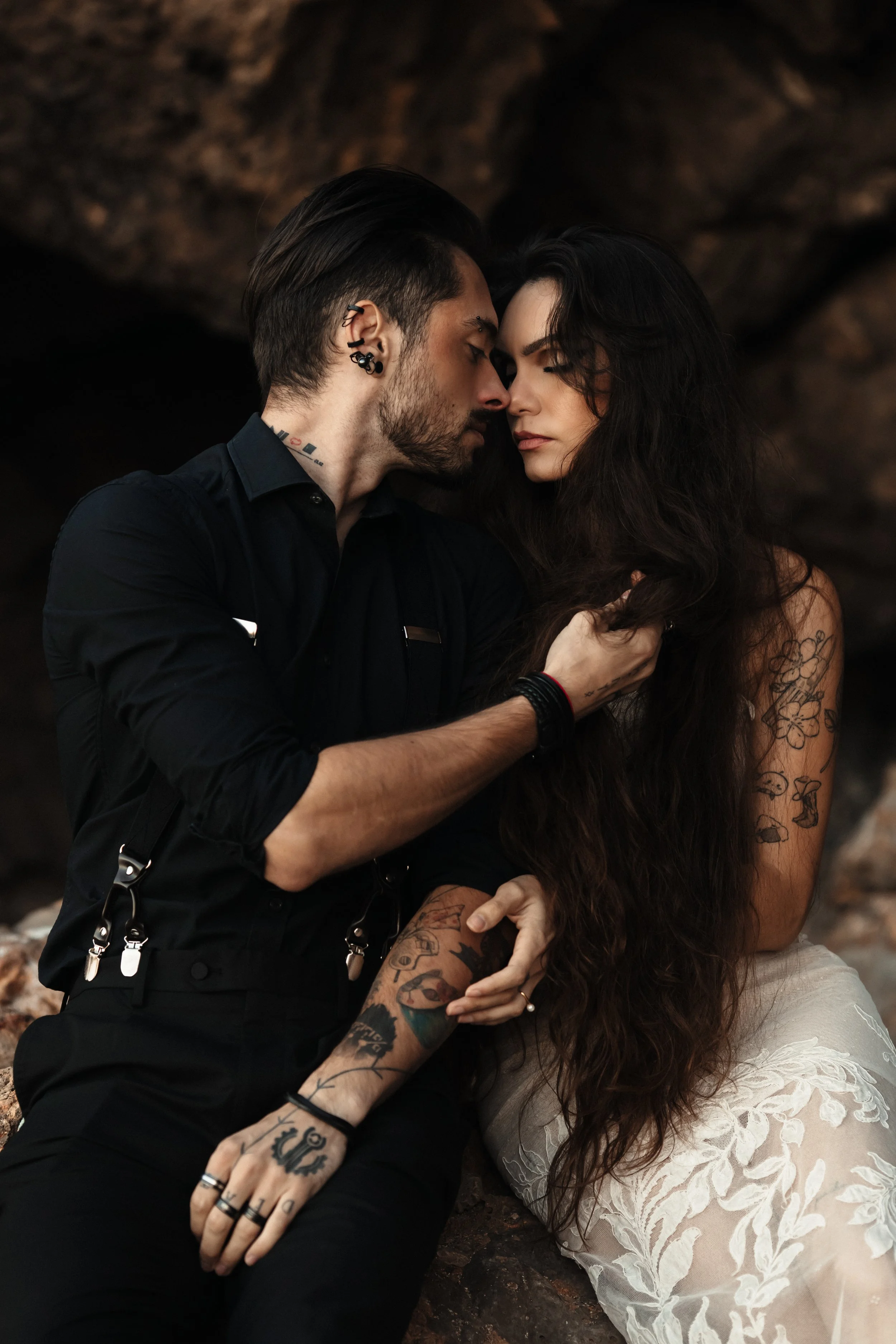 Un couple avec des tatouages, très proche, au regard intense, dans un environnement rocheux.