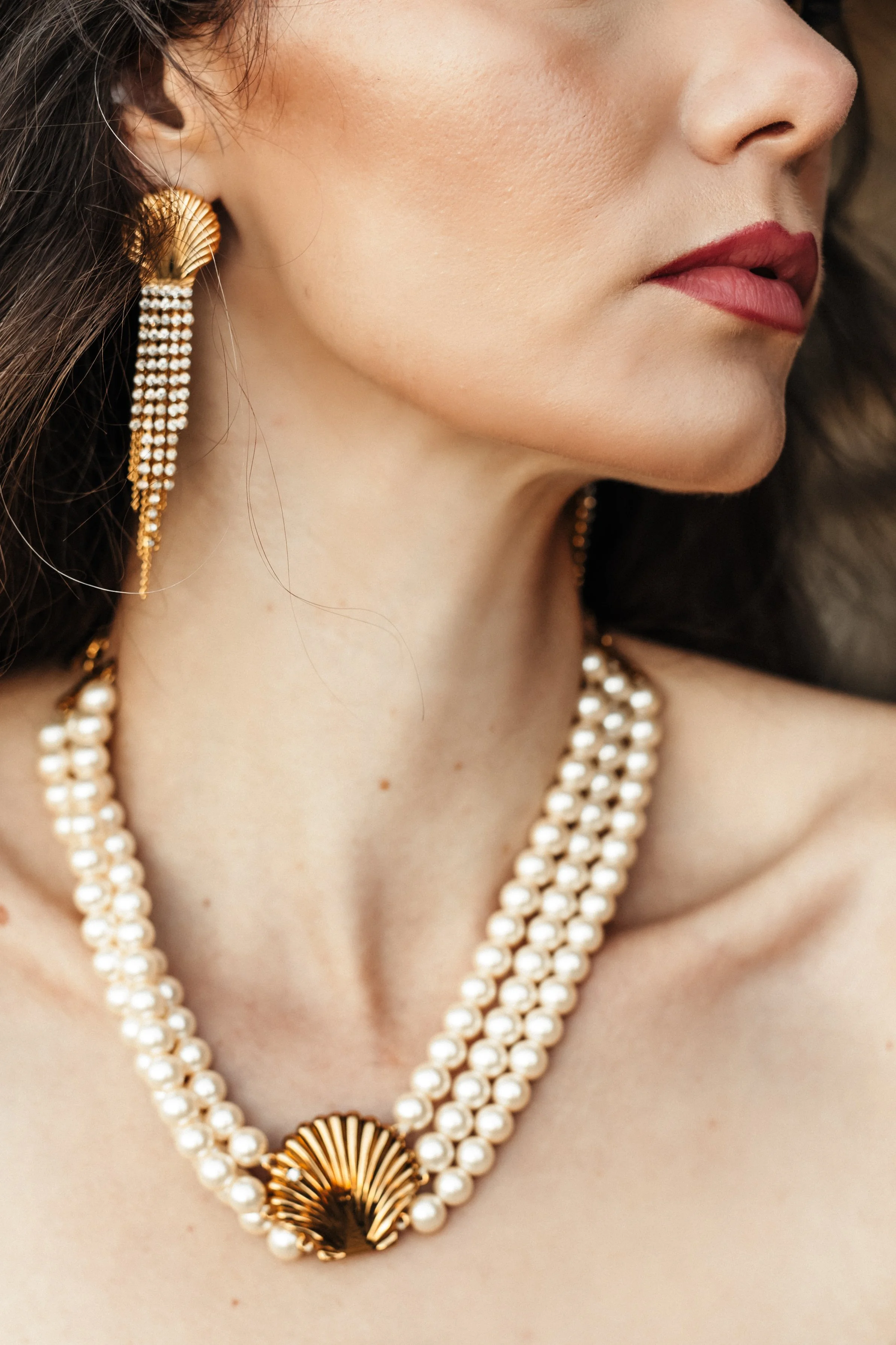 Close-up d'une femme portant des bijoux en perles avec une pièce en or en forme de coquillage.
