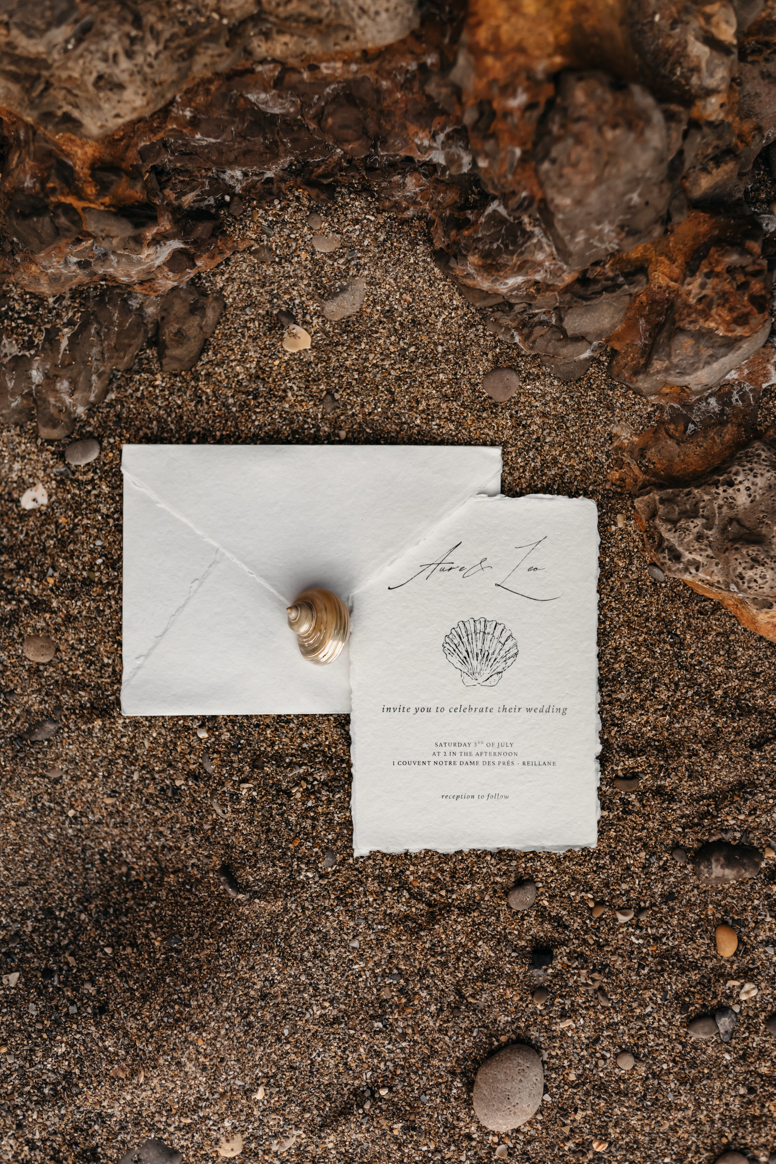 Invitation de mariage avec une coquille sur un fond de sable et de rochers.