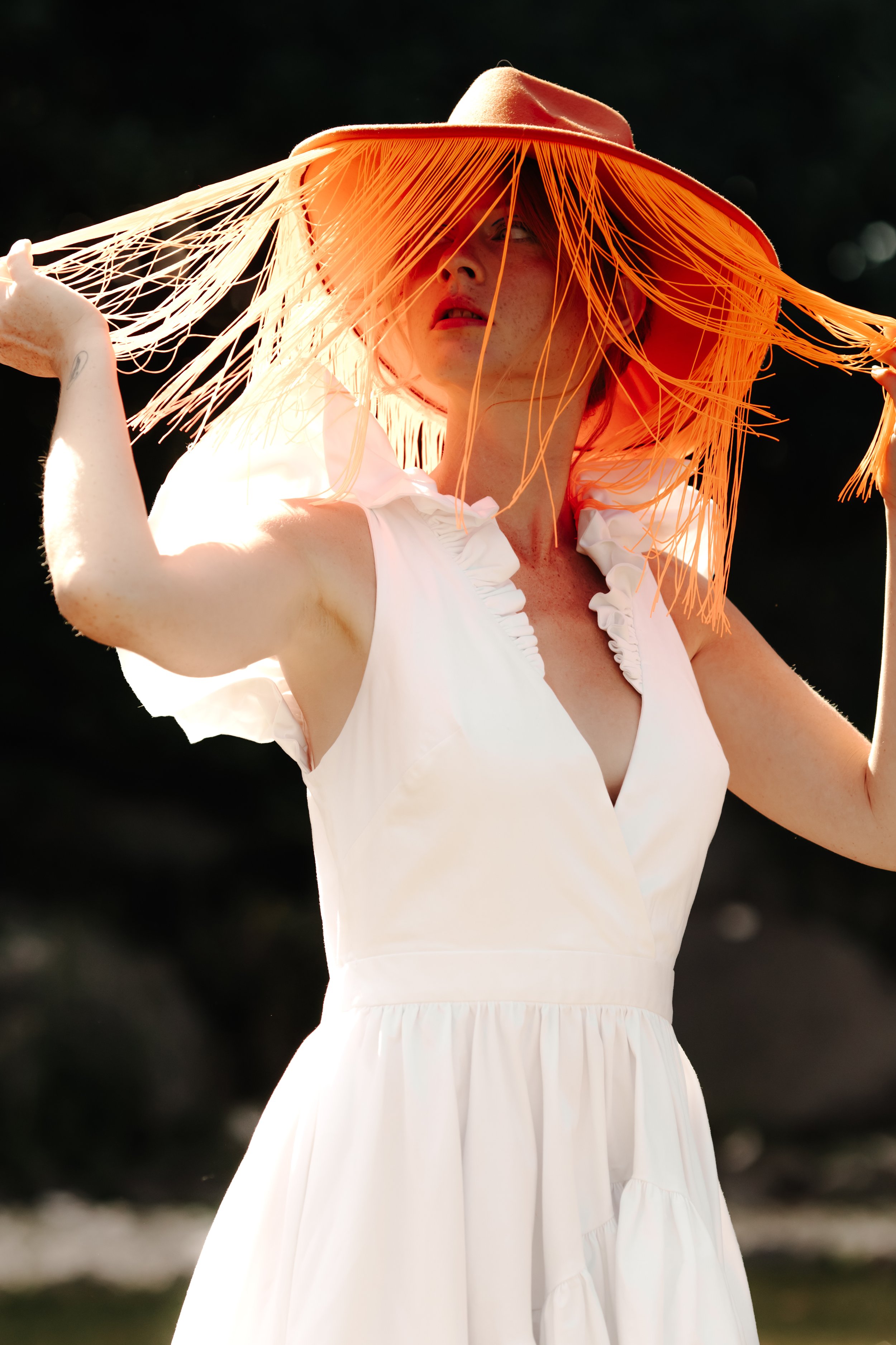 Femme portant un chapeau en paille orange avec des franges, en robe blanche, en plein air