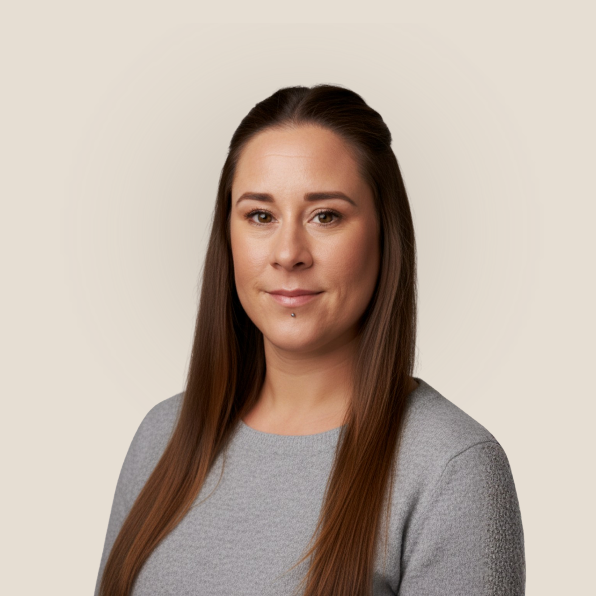 A woman with straight brown hair wearing a green top and small earrings, standing against a plain light-colored background. Her name is Rosie Bunnage