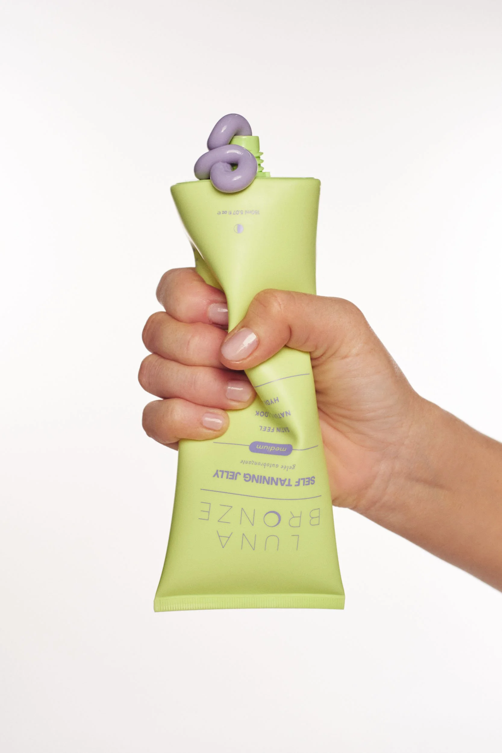 Hand squeezing bottle of purple self tanning jelly