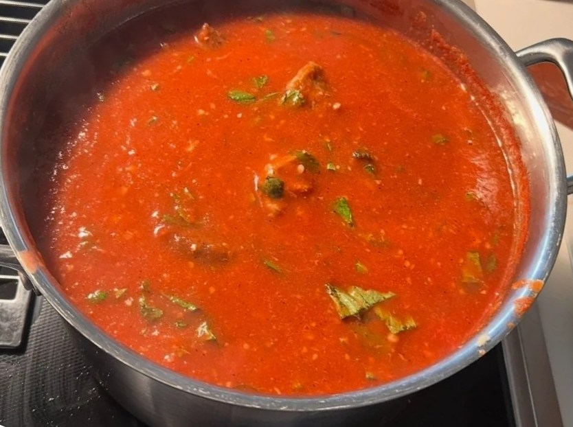 Pot of homemade tomato sauce with visible chunks of tomatoes and herbs, simmering on a stovetop.
