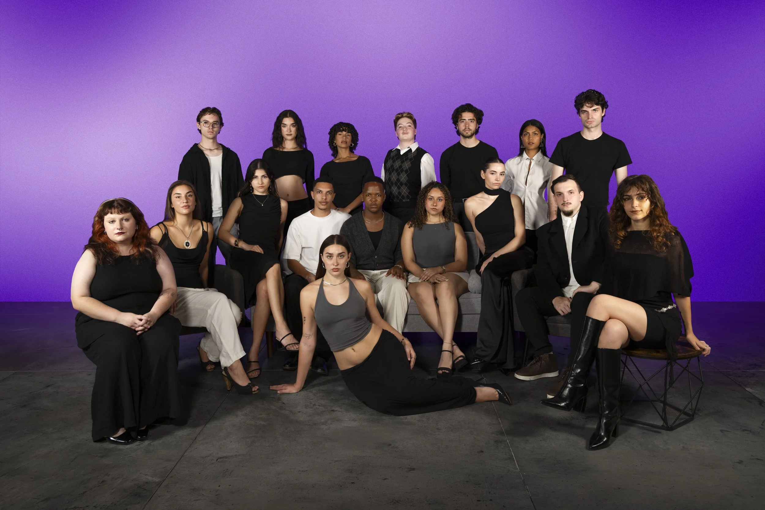 A diverse group of 16 young adults posing together against a purple background, some seated and others standing, dressed in stylish casual and semi-formal clothing.