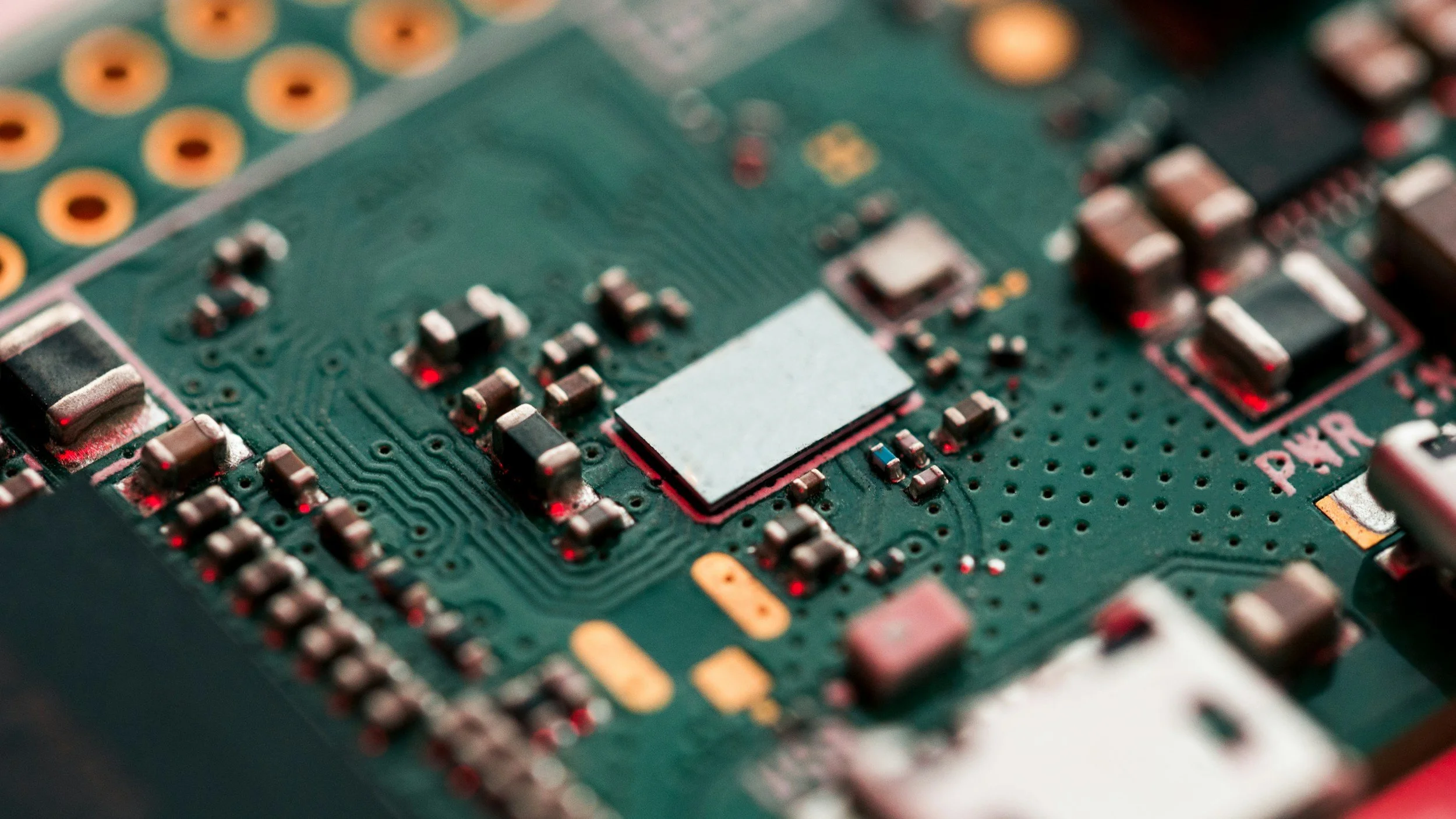 Close-up view of a green printed circuit board (PCB) with various small electronic components, including resistors, capacitors, and integrated circuits.