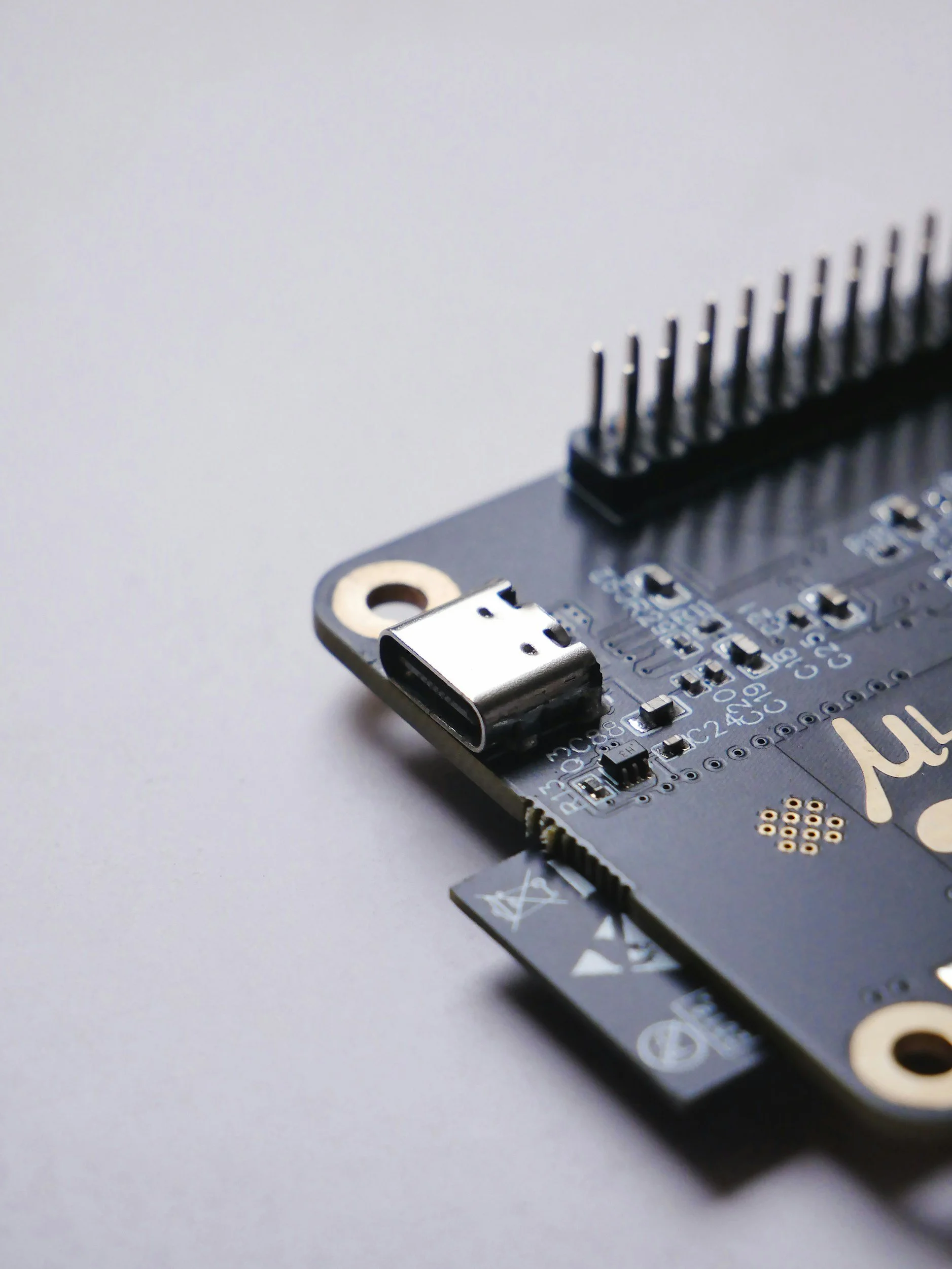 Close-up of a black microcontroller board with a USB port, pins, and various electronic components on a gray surface.