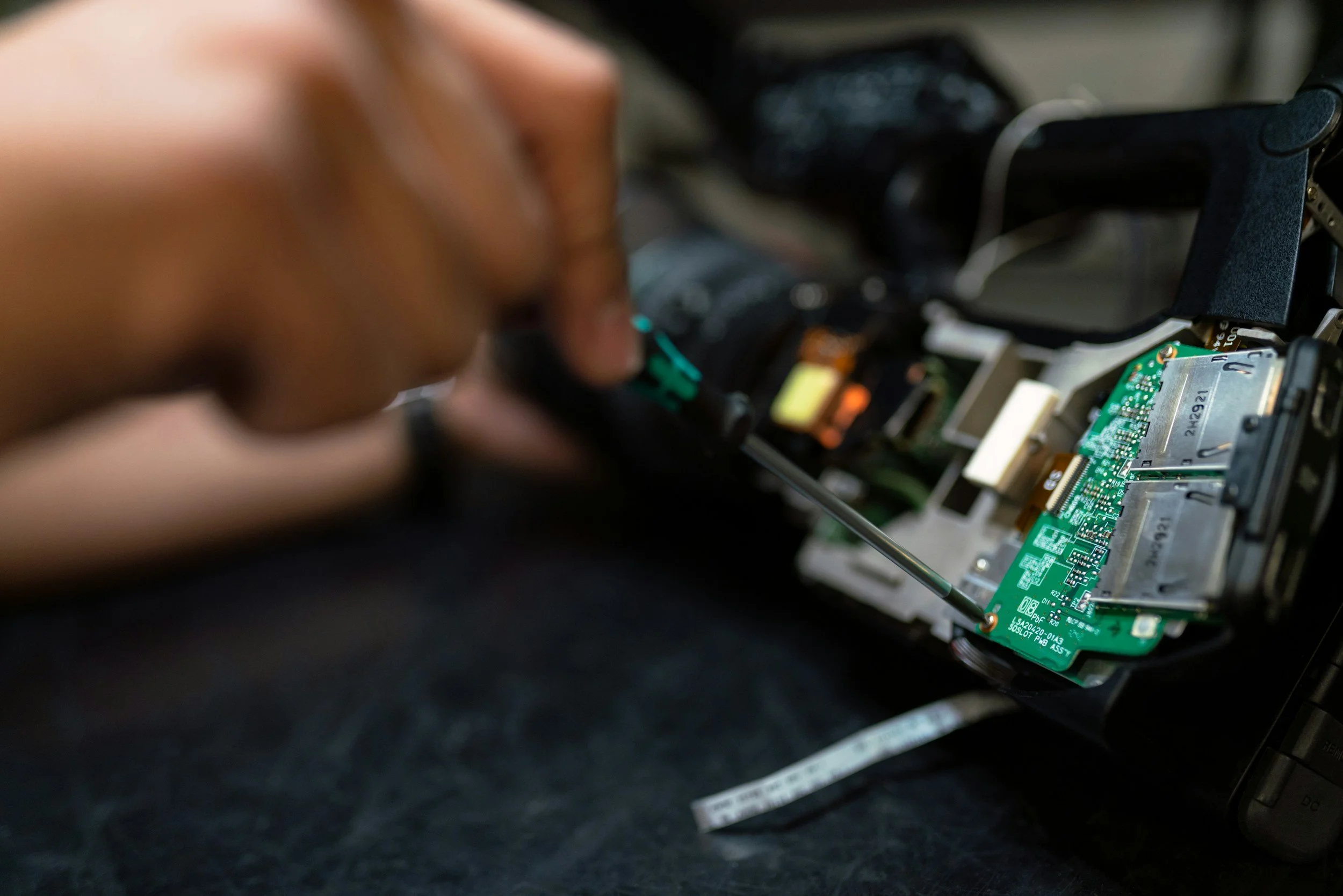 A person using a screwdriver to repair or work on a computer motherboard inside a disassembled device.