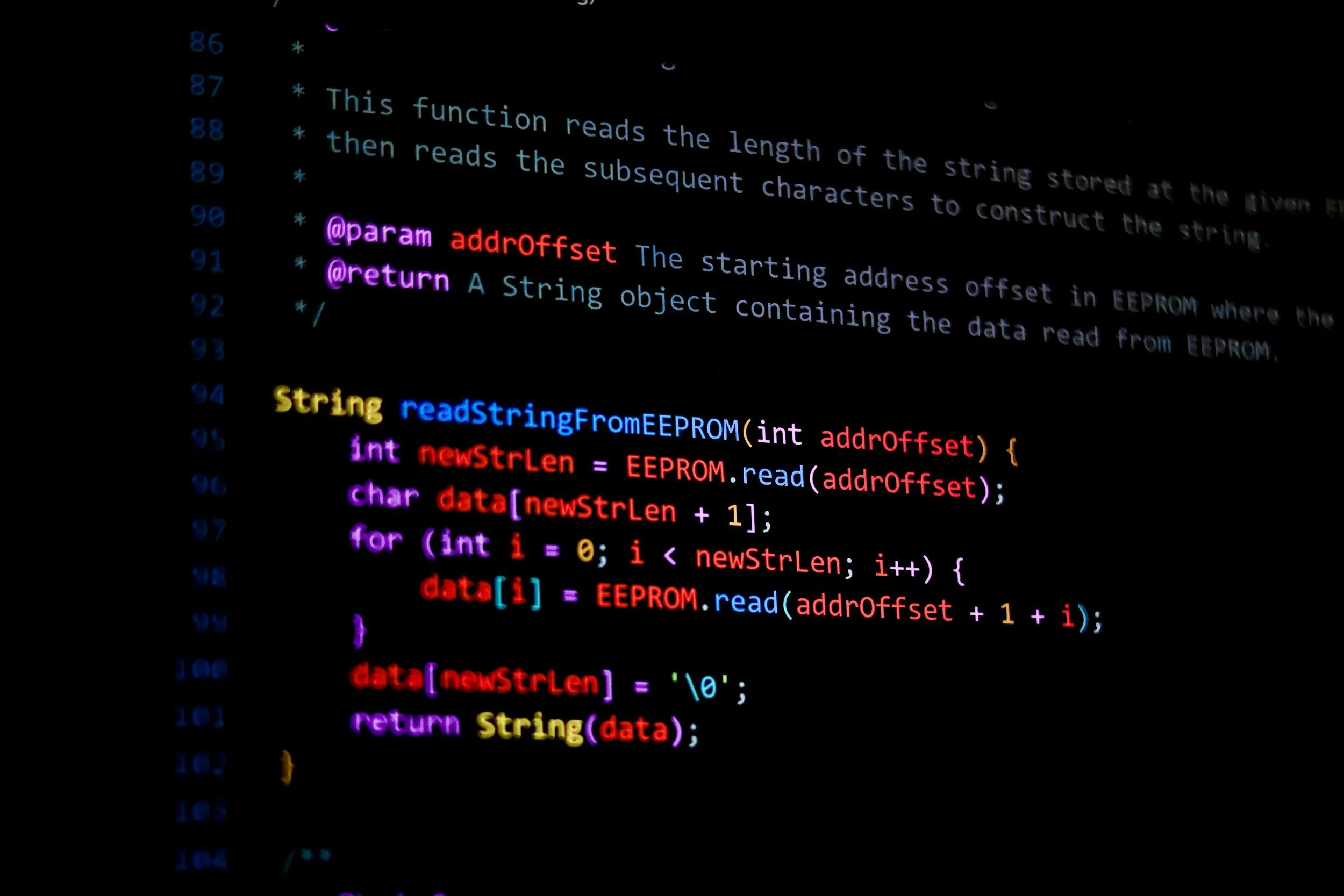 Colorful programming code on a dark screen, involving reading a string from EEPROM, with syntax highlighted in yellow, blue, purple, red, and pink.