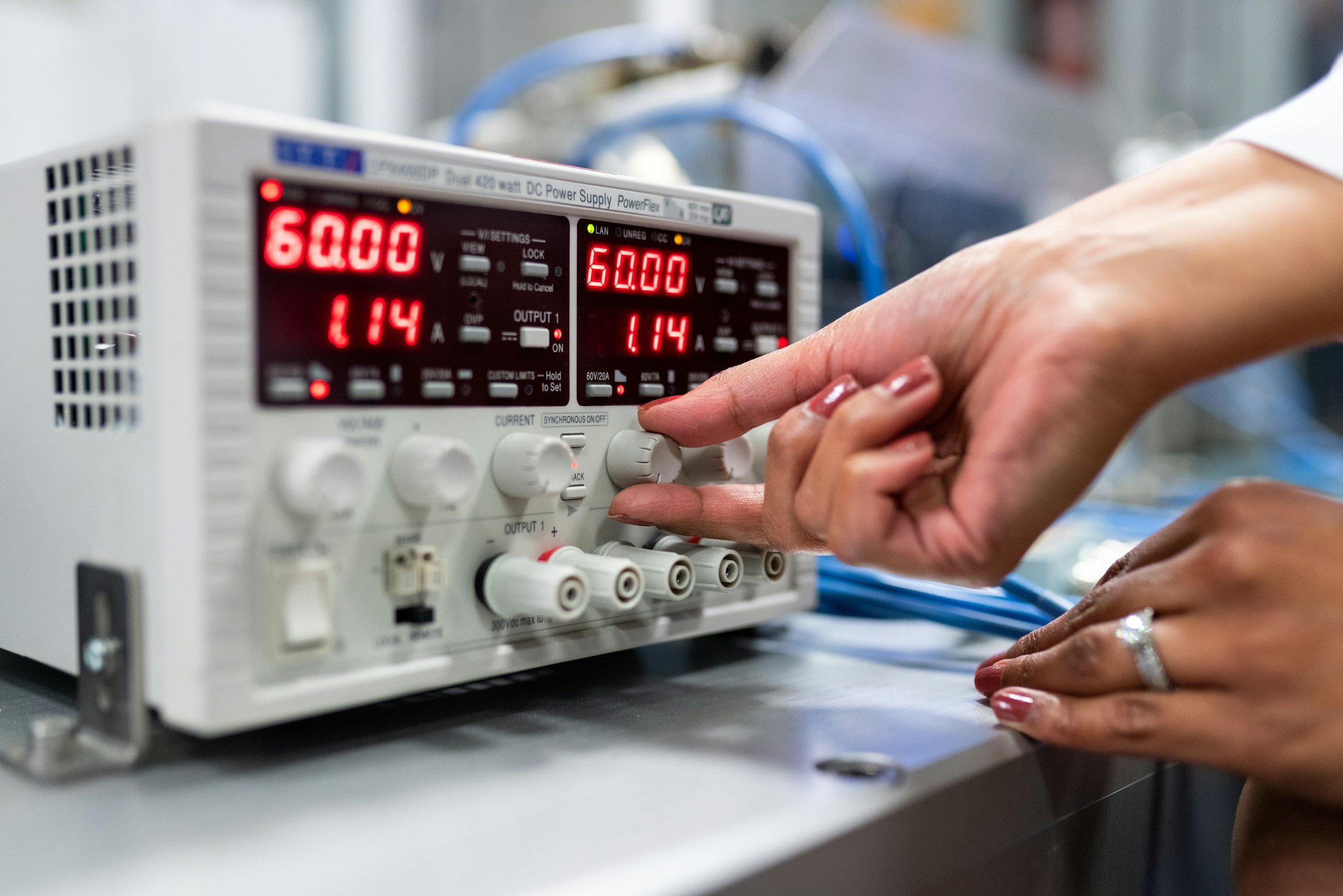 Person adjusting settings on a laboratory power supply with digital displays showing voltage and current.