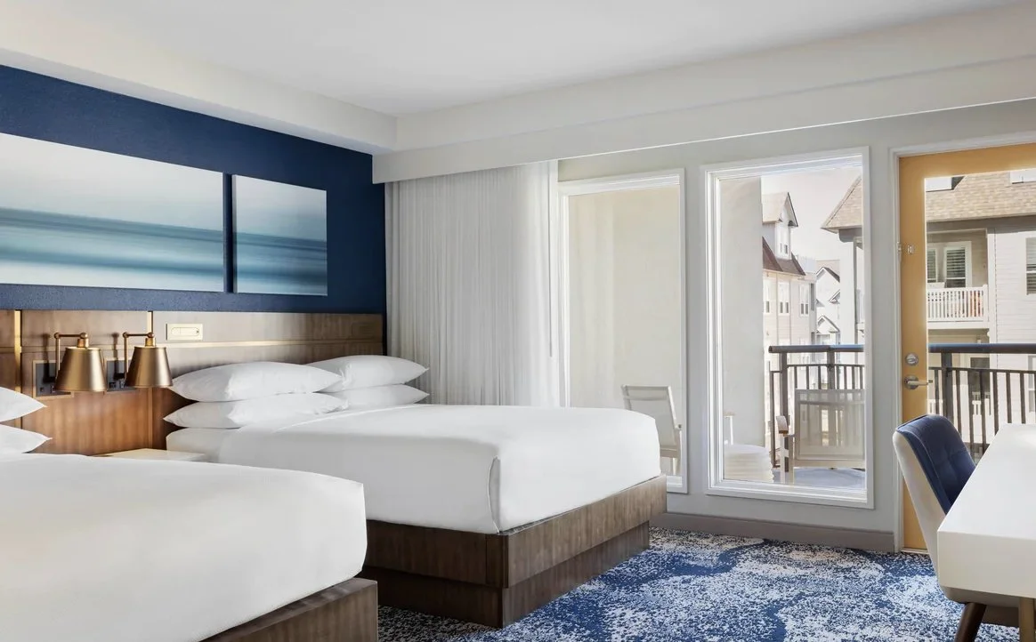Hotel room with two white beds, a balcony door, and ocean view painting