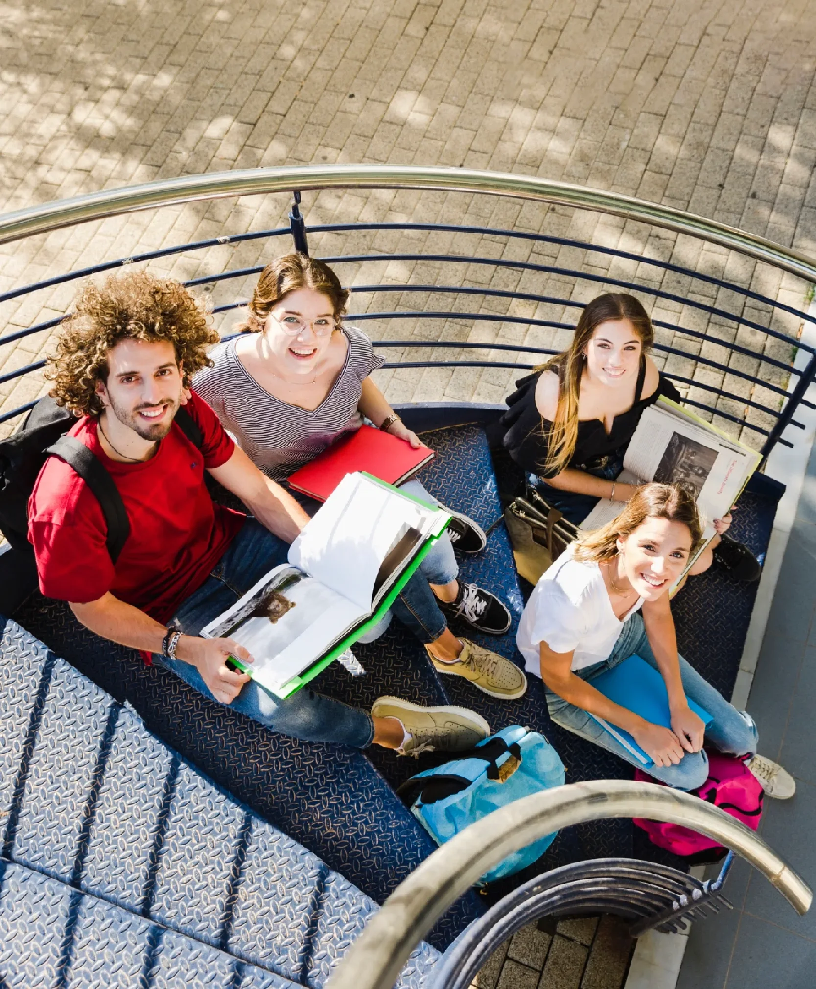 Group of four university students sitting together with books and notebooks, smiling and looking upward, representing Universal Human Foundation's support for students in education and emotional wellbeing.