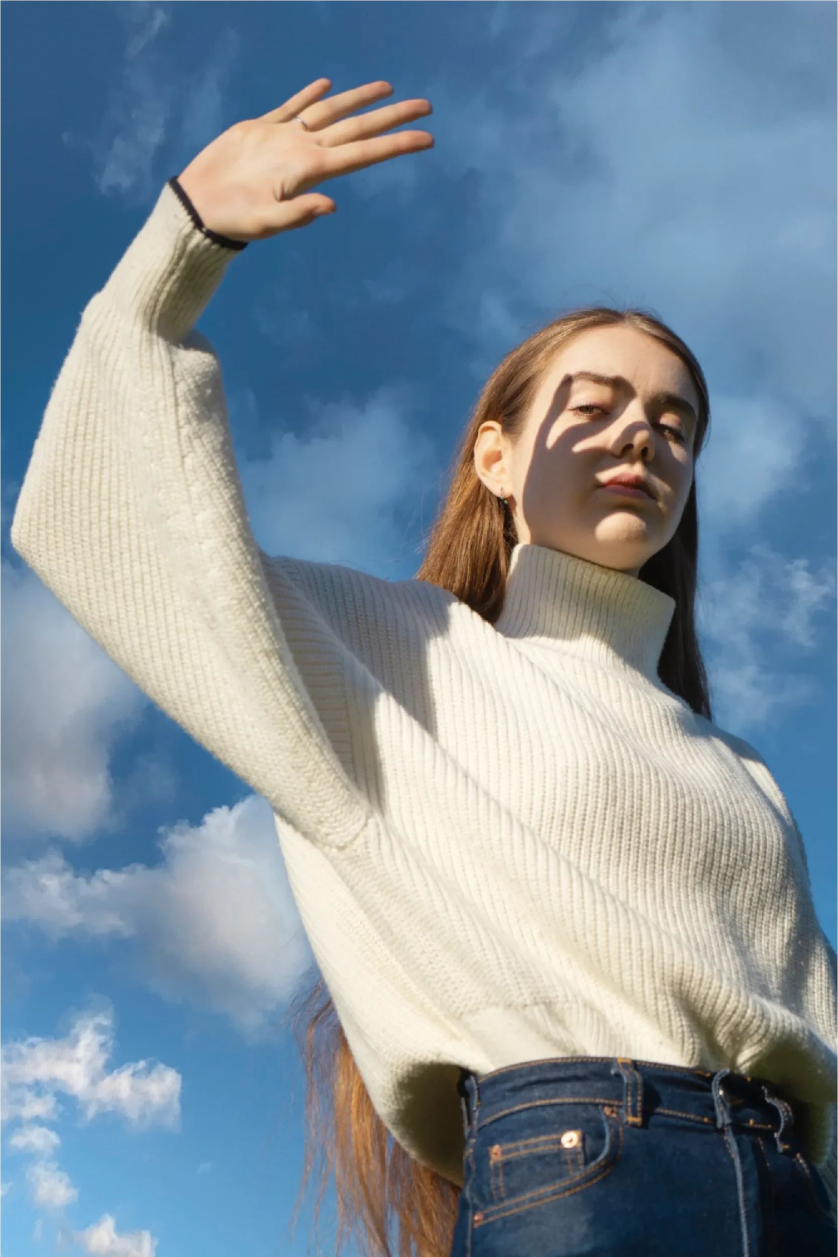 Young woman in a white sweater with her arm raised against a bright blue sky, representing Universal Human Foundation's support for empowerment, confidence, and personal aspiration.