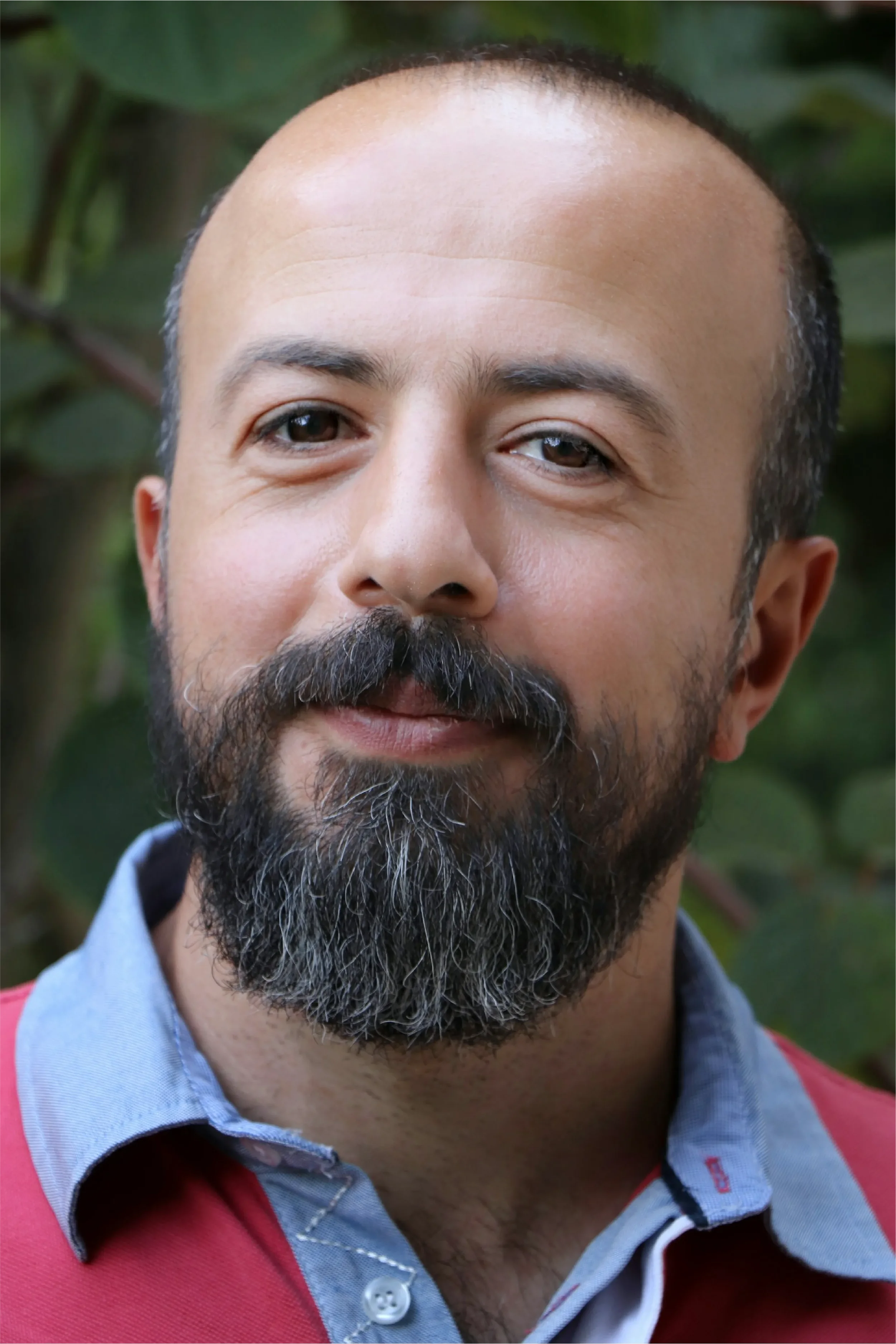 Close-up portrait of a middle-aged man with a full beard smiling gently, representing Universal Human Foundation's support for inner wisdom, reflection, and authentic connection.