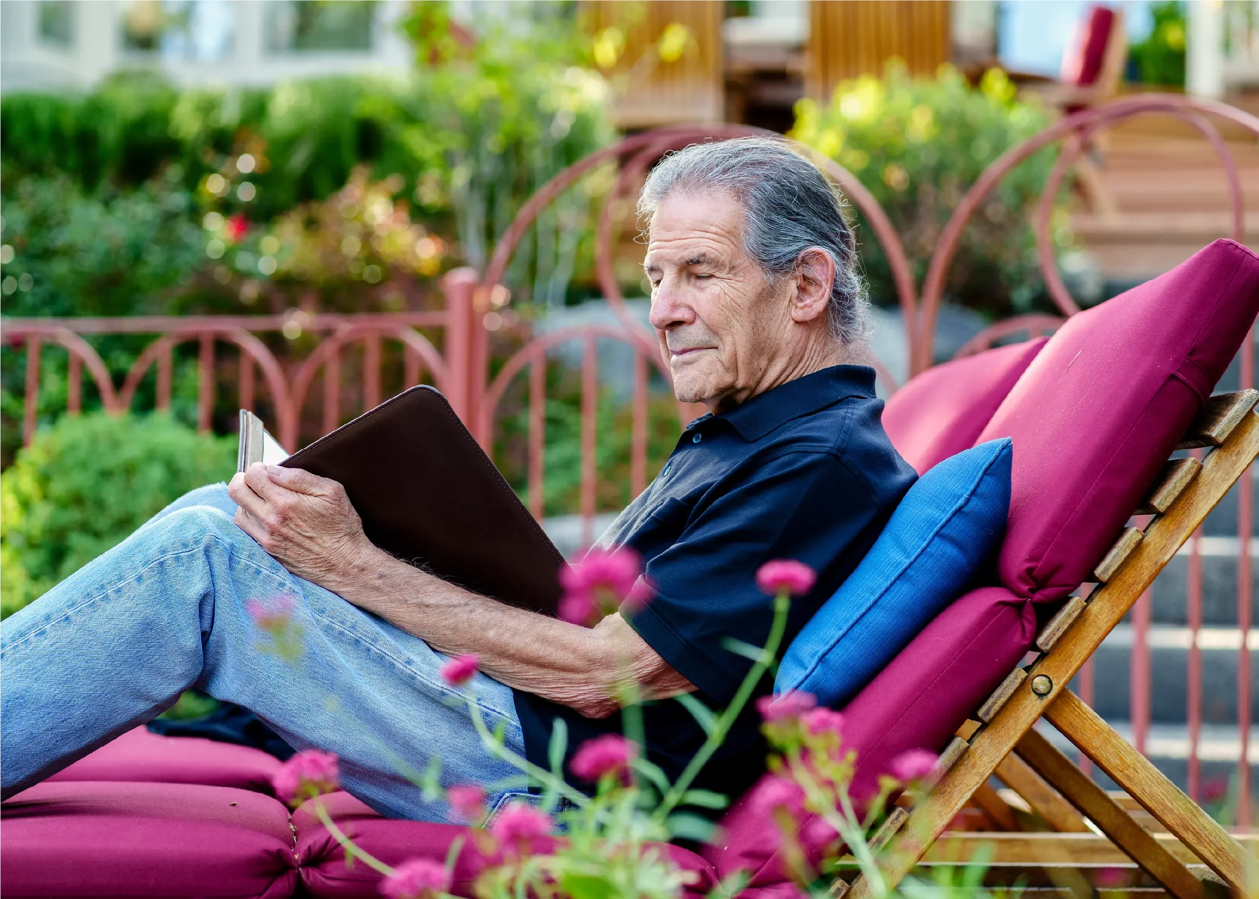Gary Zukav, author and co-founder of Seat of the Soul Institute, reading peacefully in a garden chair surrounded by pink flowers, embodying reflection and contemplation.