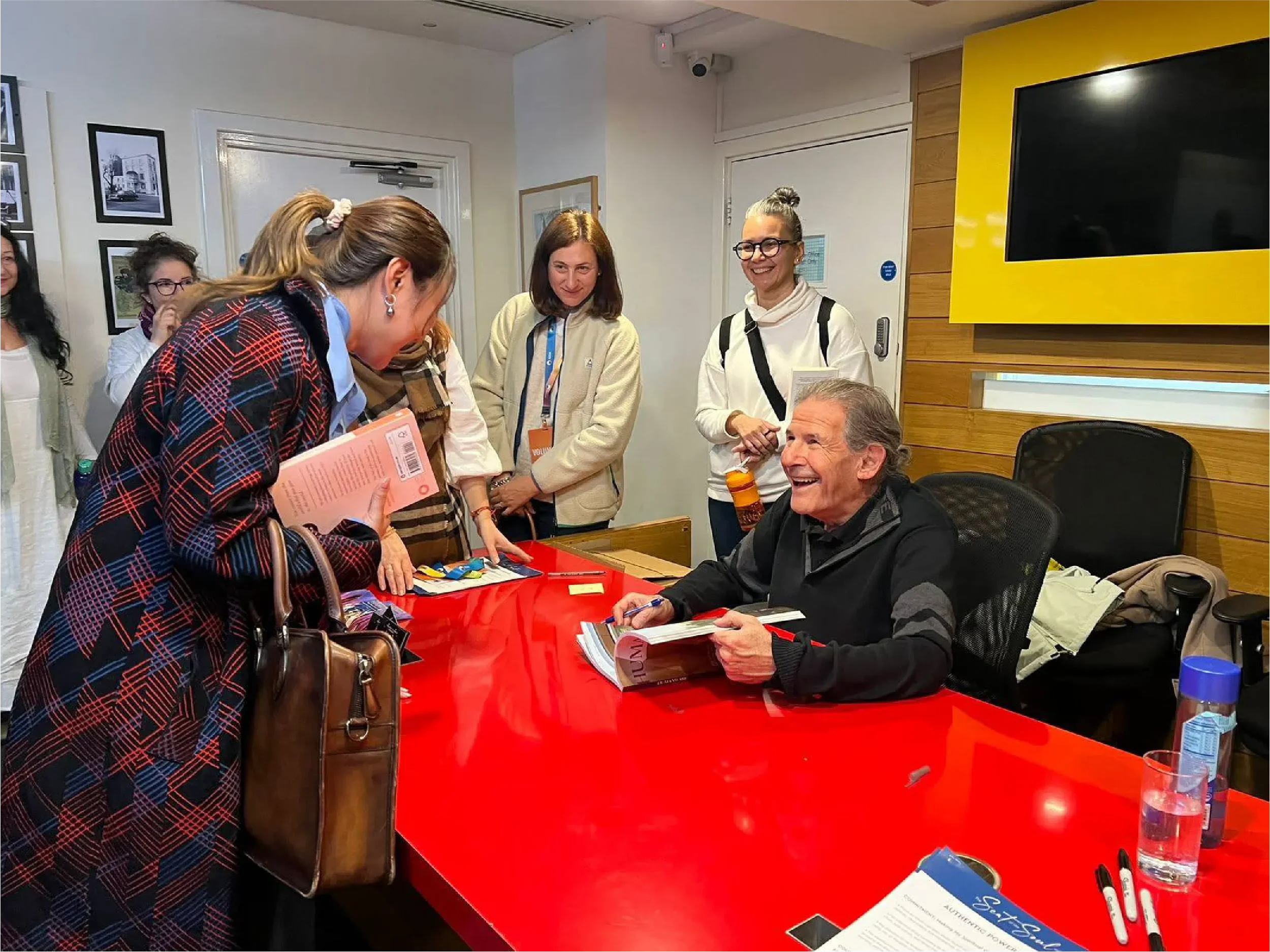 Gary Zukav laughing joyfully while signing copies of his book "Universal Human" at a book event, with readers gathered around, sharing in a warm community moment supported by Universal Human Foundation.