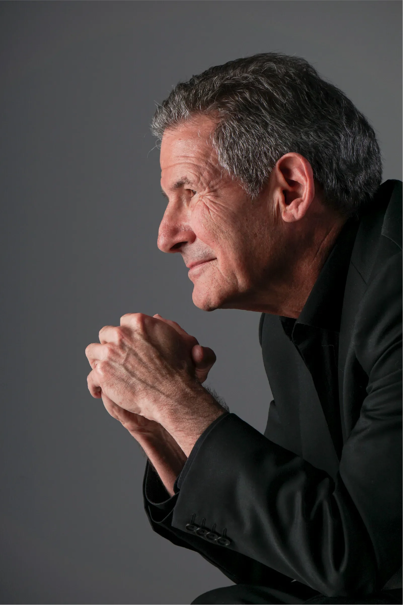 Gary Zukav in profile, resting his hands together and looking forward with a calm and reflective expression, conveying contemplation, wisdom, and inner awareness