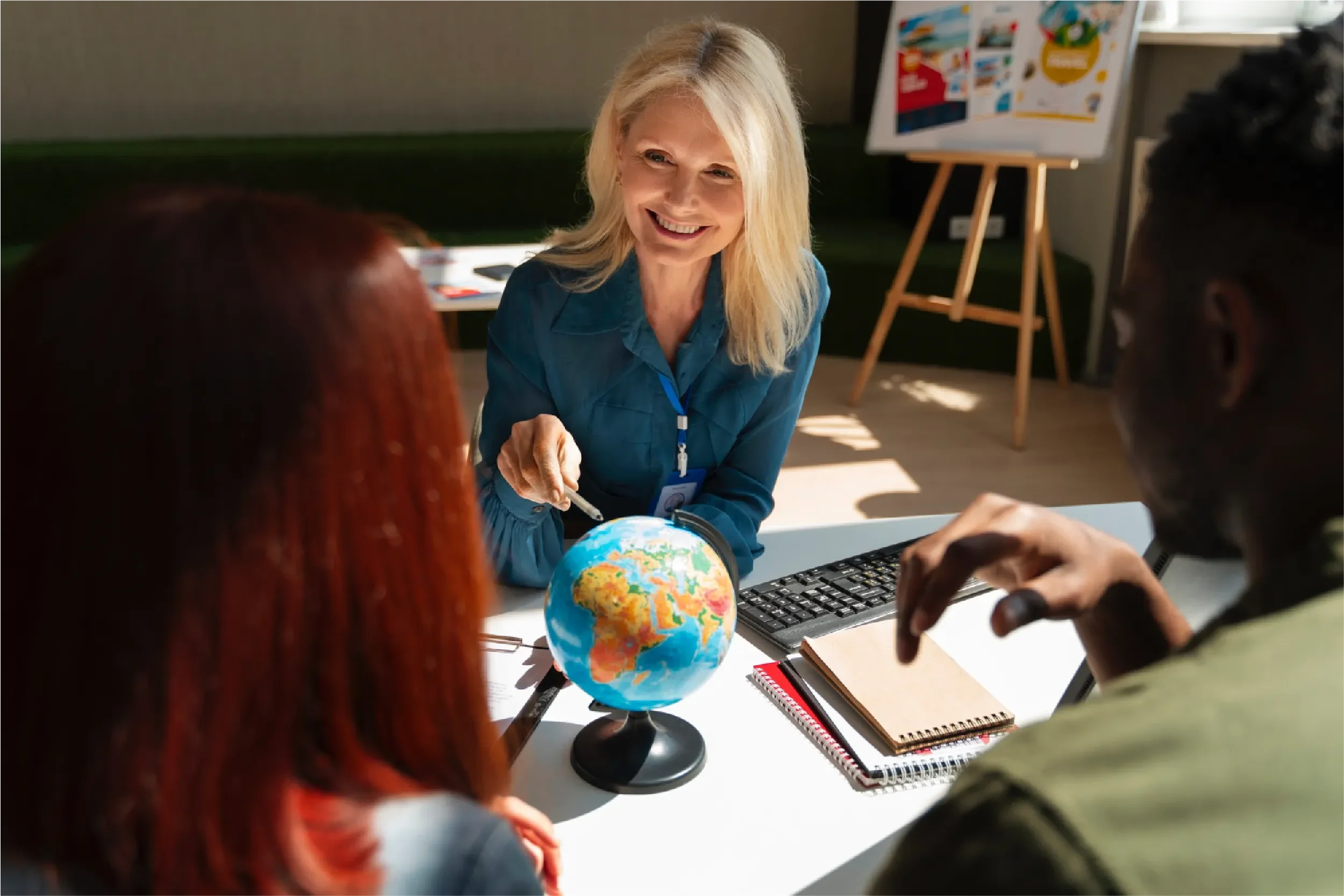 Smiling teacher pointing to a world globe while engaging with students in a classroom setting, representing Universal Human Foundation's support for education, global awareness, and meaningful learning.