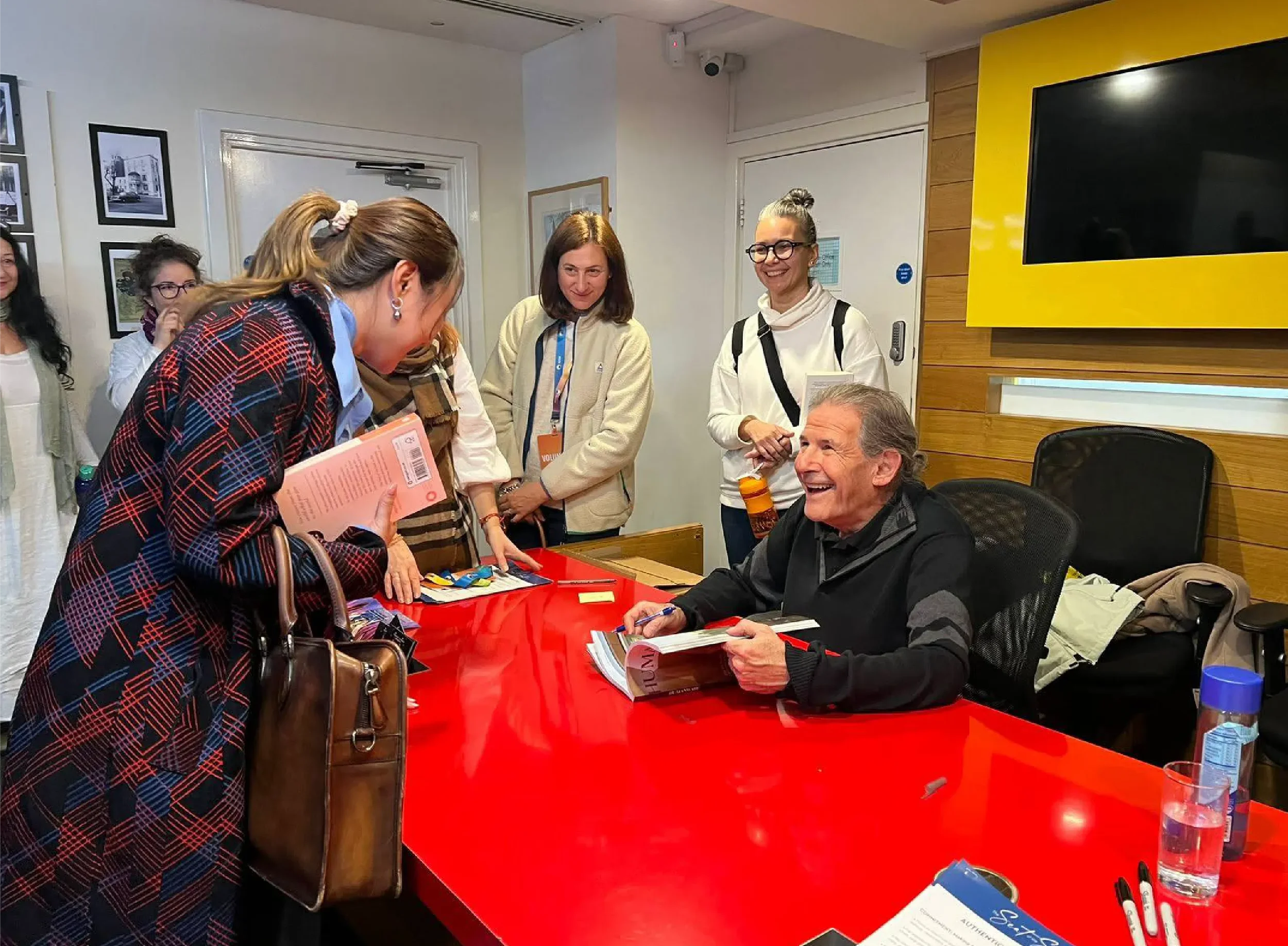 Gary Zukav laughing joyfully while signing copies of his book "Universal Human" at a book event, with readers gathered around, sharing in a warm community moment supported by Universal Human Foundation.