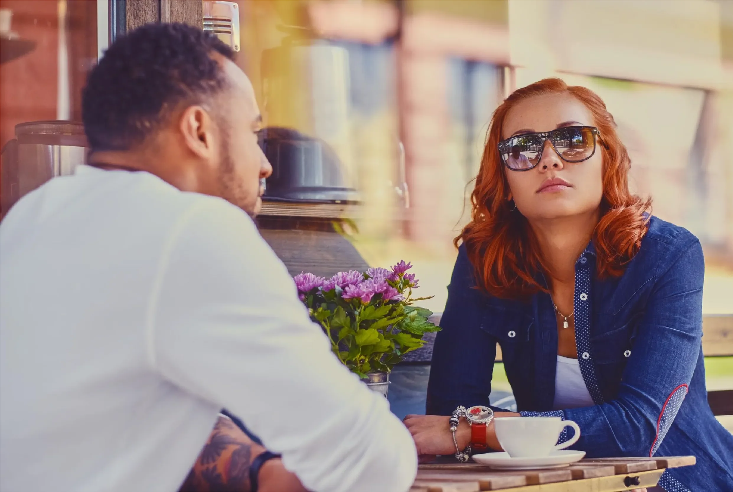 Couple sitting at an outdoor café having a tense conversation, with a woman in sunglasses looking serious, representing Universal Human Foundation's support for navigating difficult relationship dynamics and emotional communication.