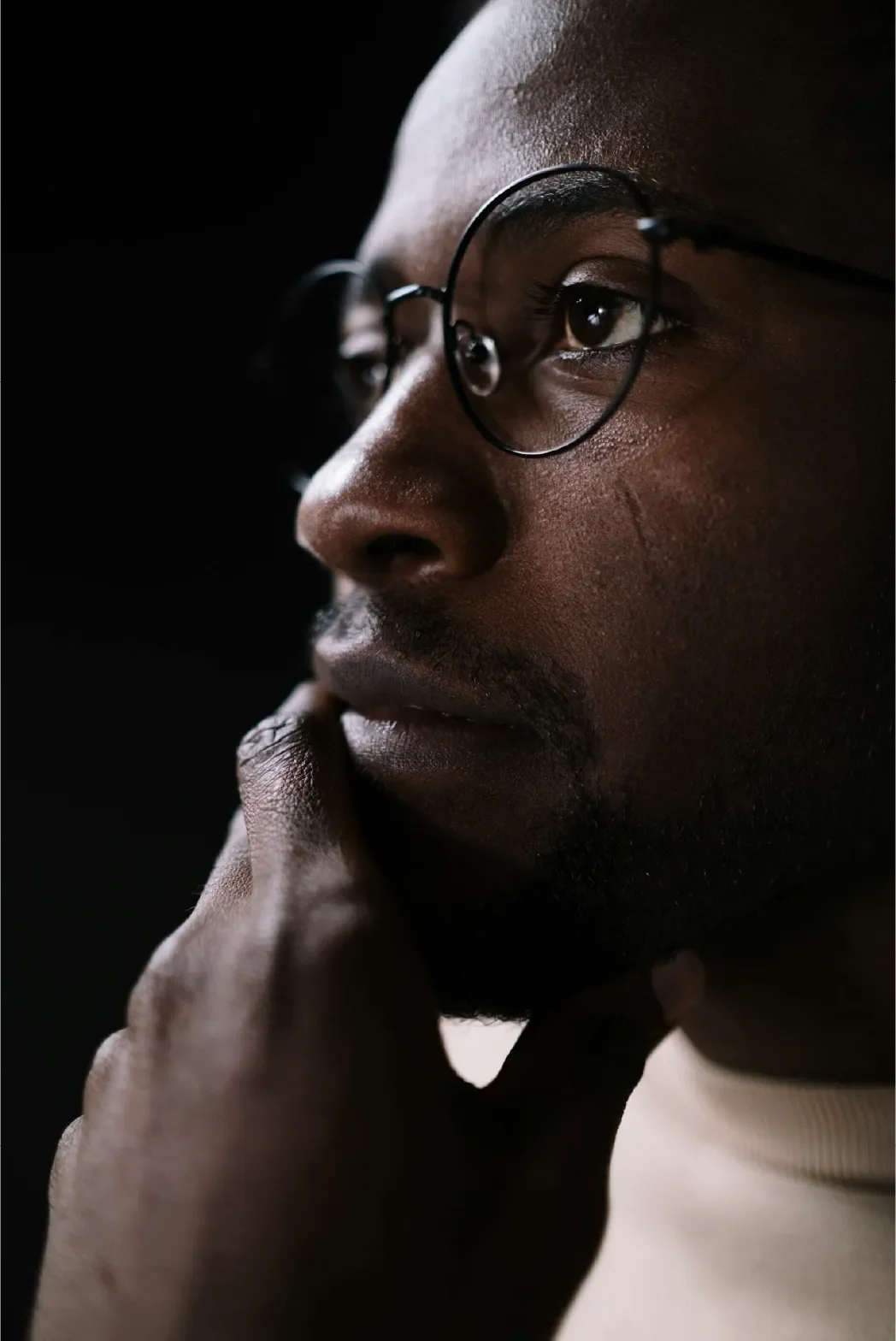 Thoughtful profile portrait of a young Black man with glasses gazing into the distance, representing Universal Human Foundation's support for inner reflection, contemplation, and personal growth.