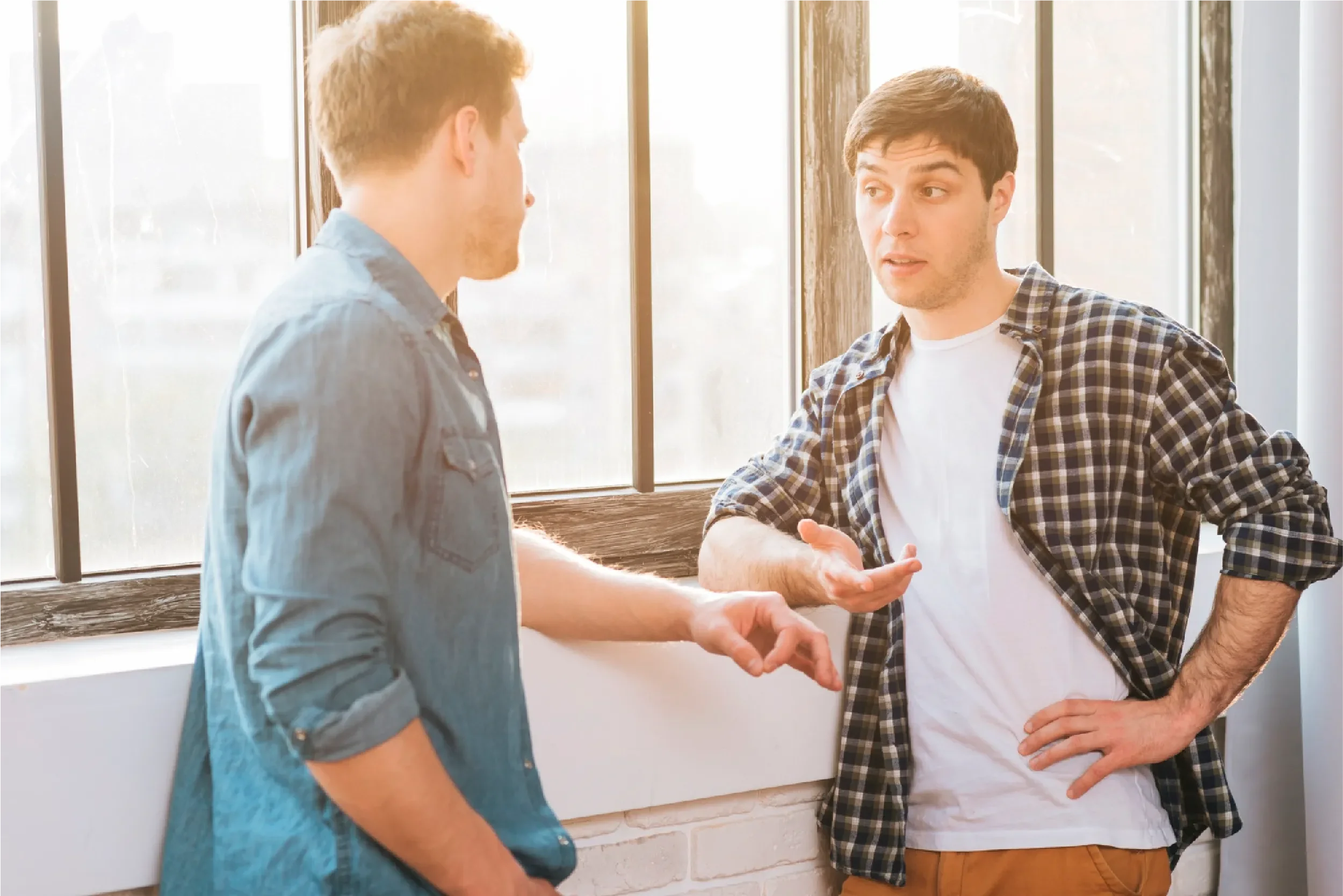 Two young men having an engaged conversation by a sunlit window, representing Universal Human Foundation's support for healthy communication and authentic connection.