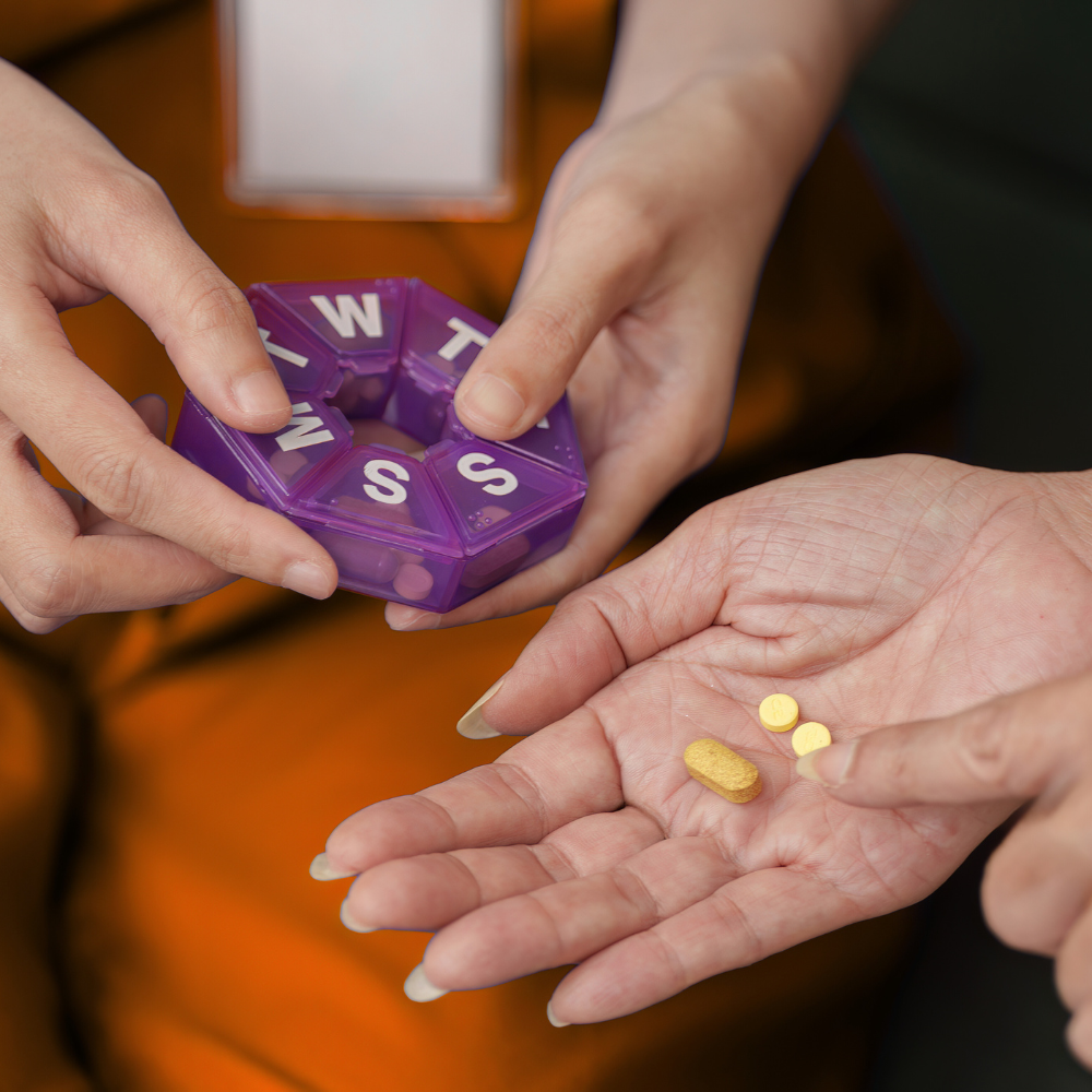 Two people exchanging prescription medication and a pill organizer with purple compartments labeled with days of the week.