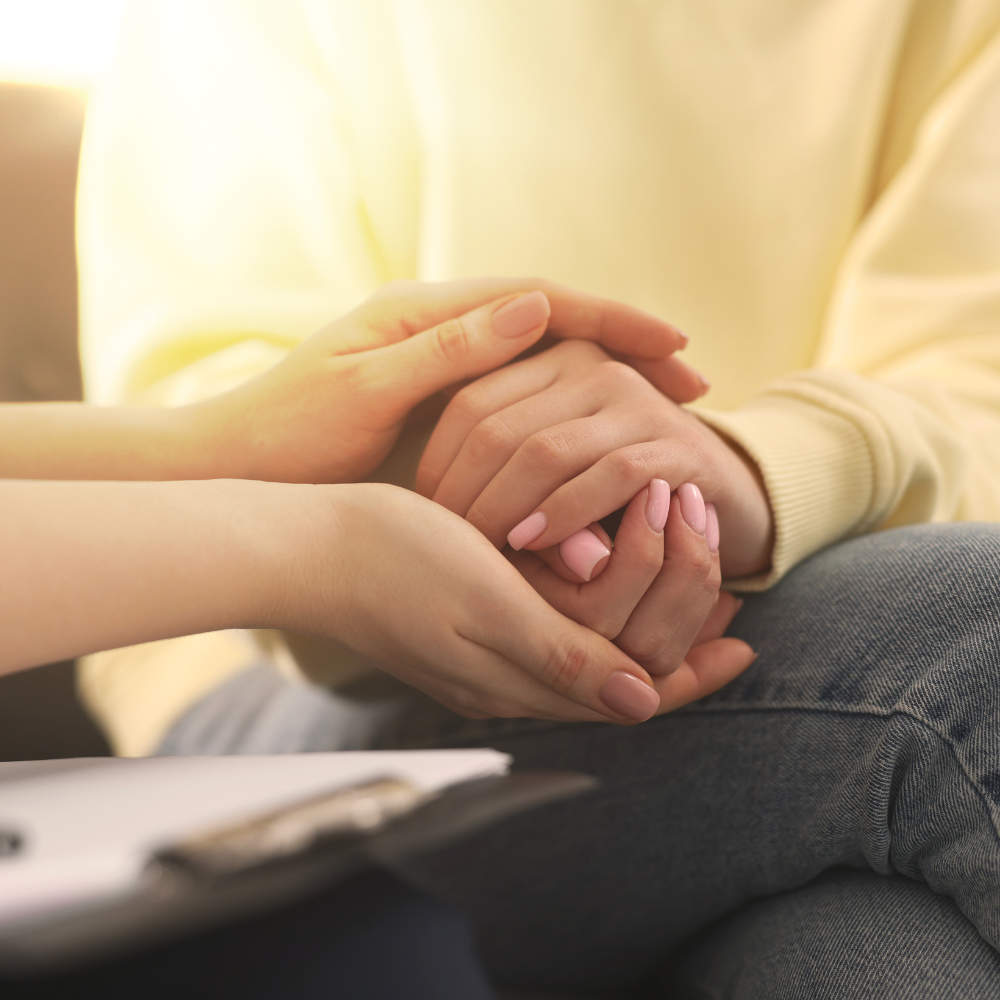 A person in a yellow sweater holding hands with another person, showing support and comfort.