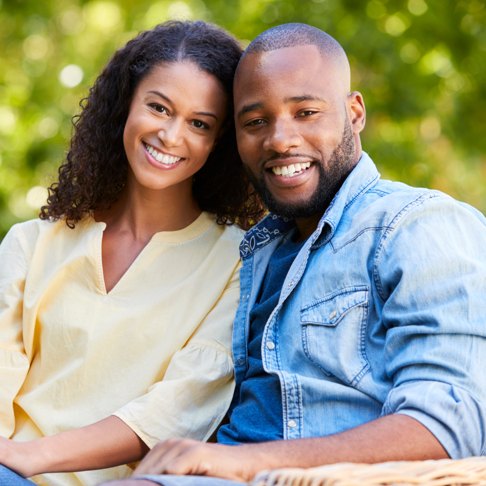 Smiling couple sitting outdoors in a park with green blurred background.