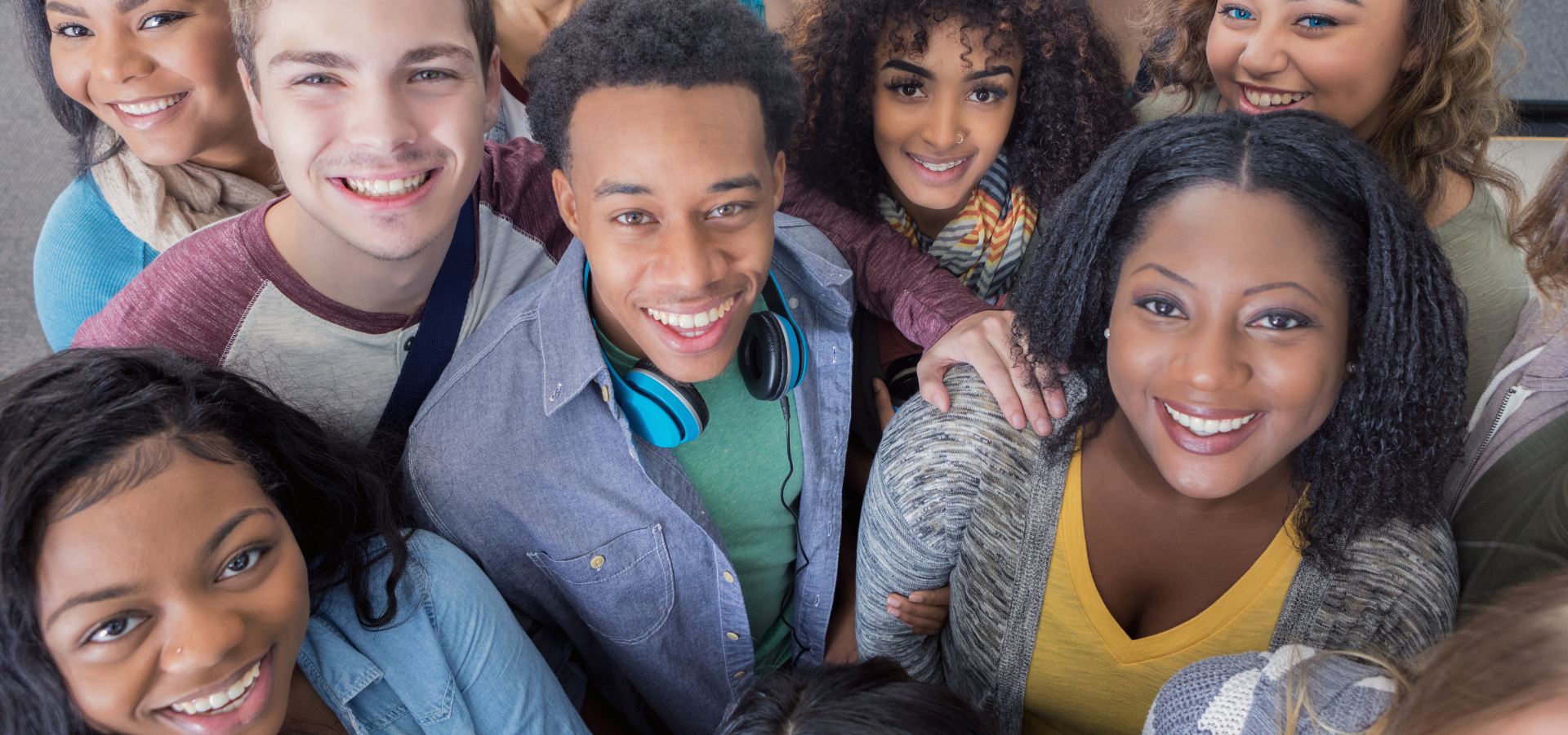 A diverse group of smiling young people, including men and women of different ethnicities, looking up at the camera.