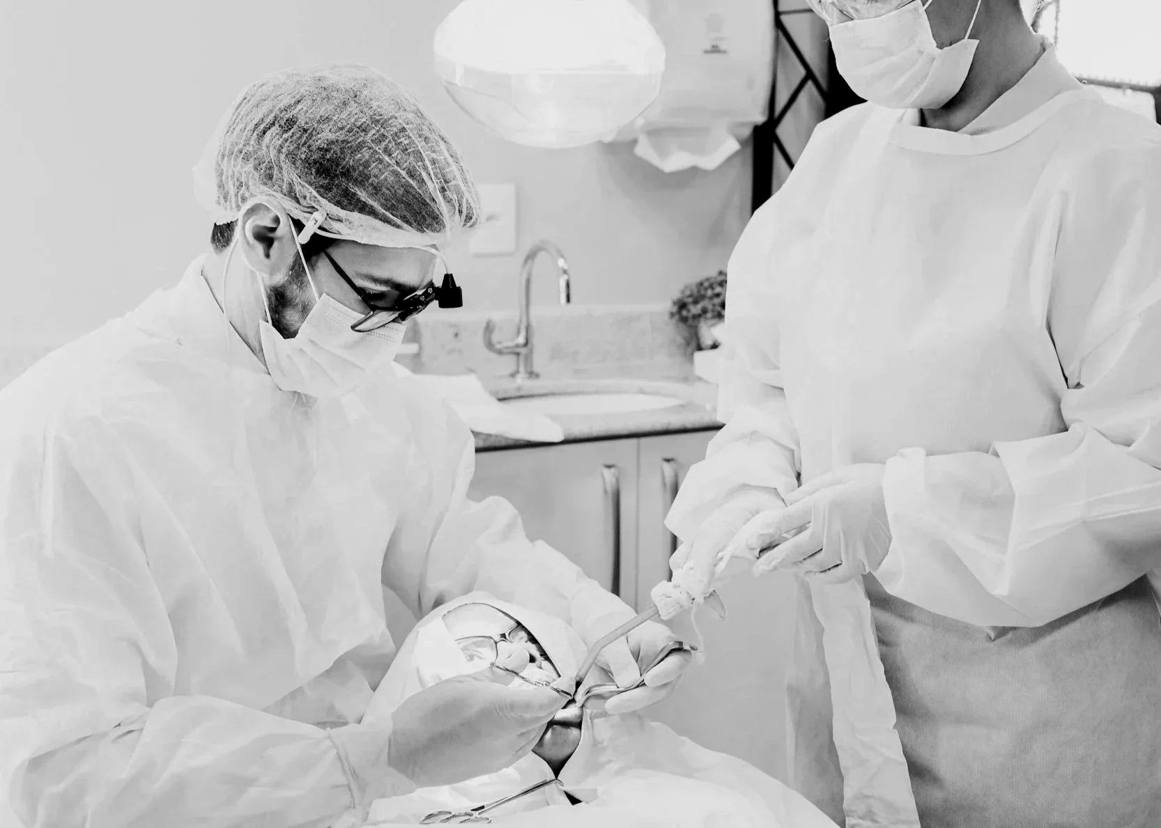 Two healthcare professionals in protective gowns and masks perform a dental procedure in a clinical setting.