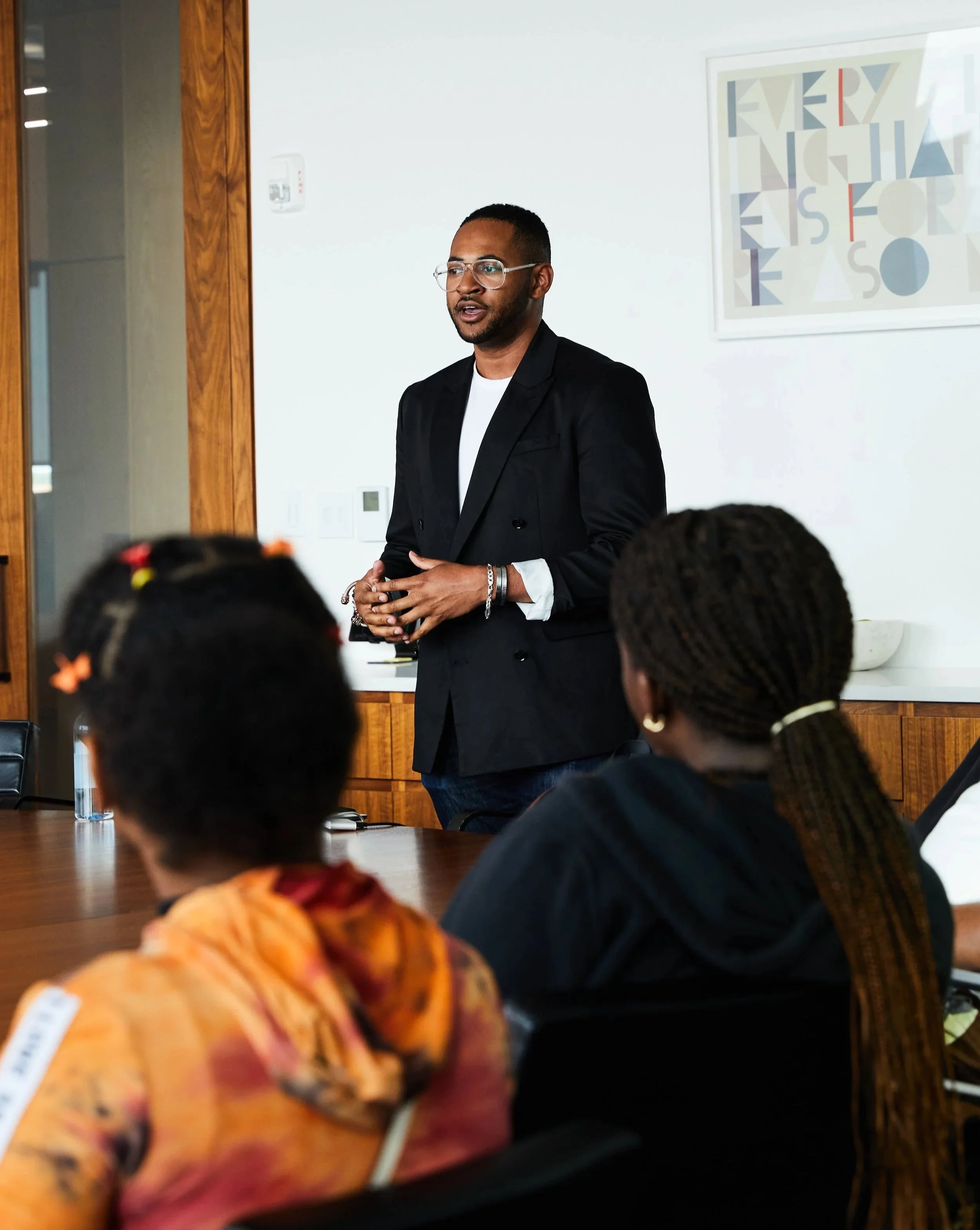 A man giving a presentation in a conference room with three women in the audience.