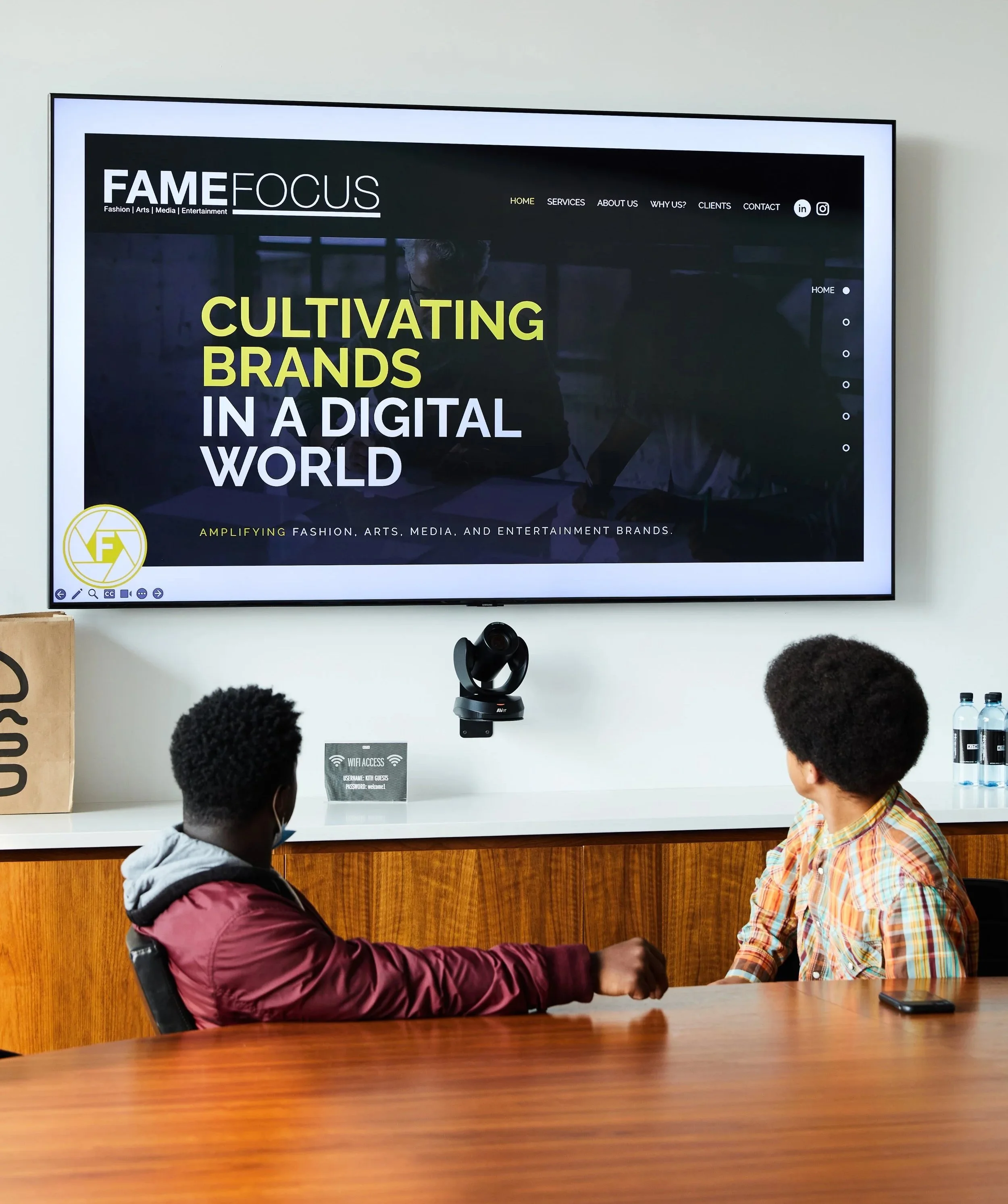 Two children are sitting at a table watching a presentation on a large screen in a modern conference room. The presentation reads 'Cultivating Brands In a Digital World'.
