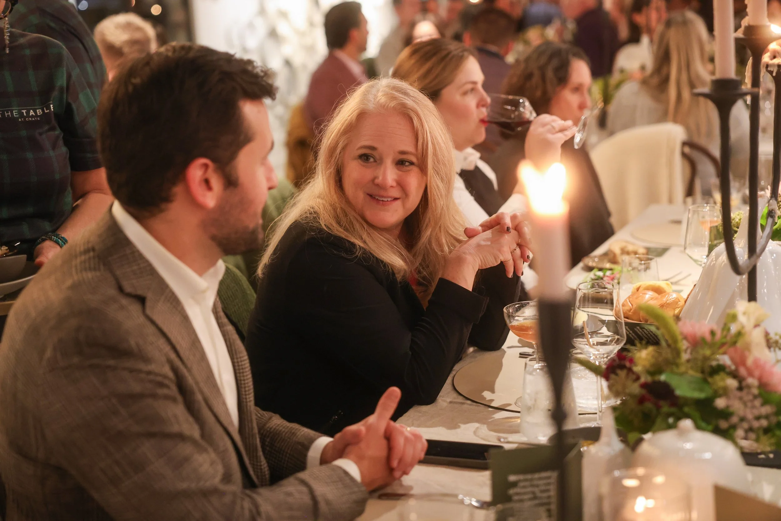 People sitting at a decorated banquet table, engaged in conversation and enjoying drinks at a lively dinner event.