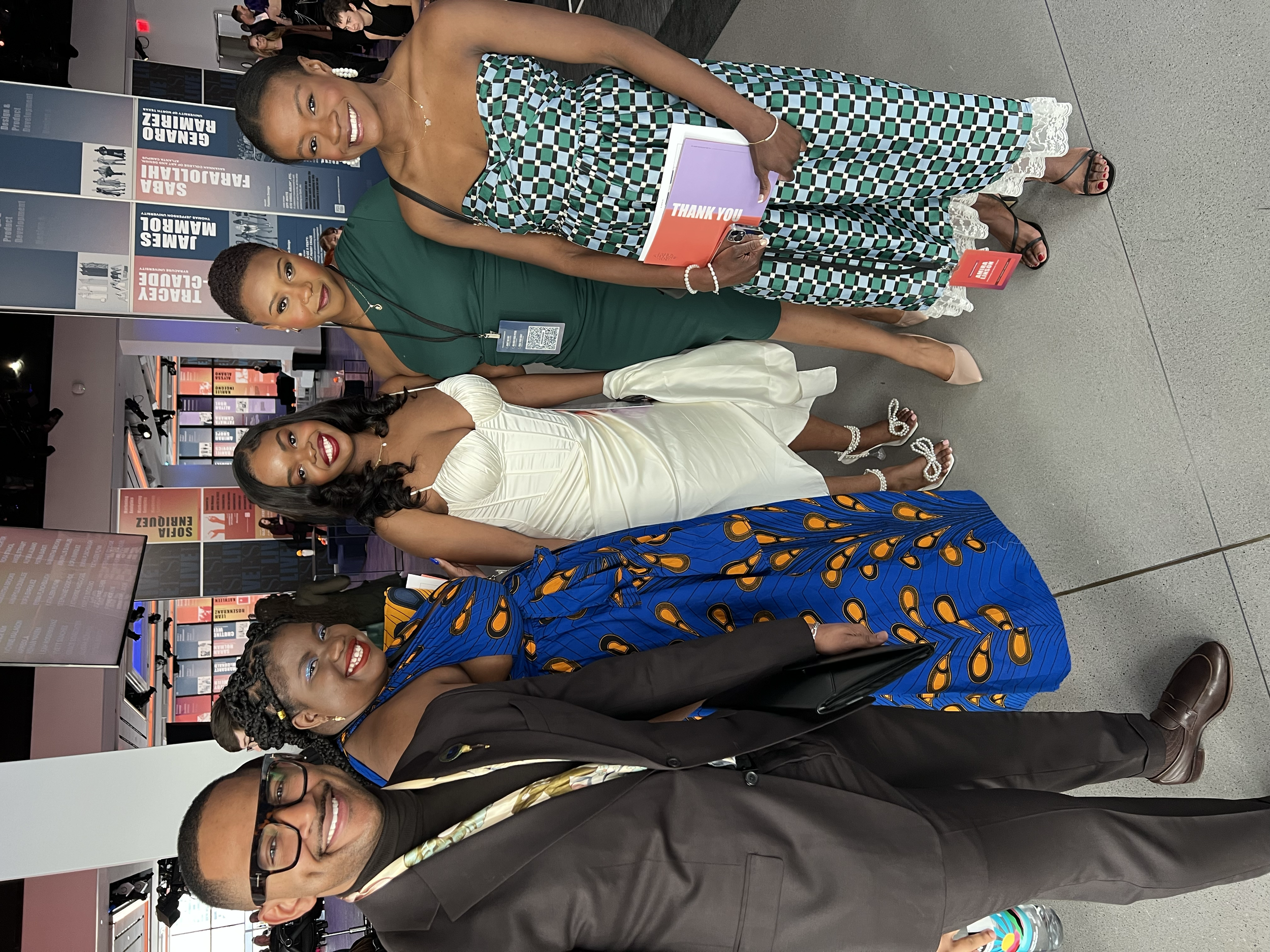 Four people, three women and one man, dressed in formal attire, standing together at an event, smiling at the camera.