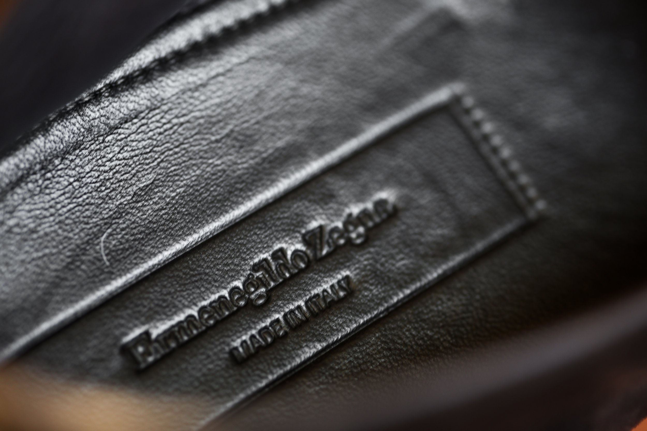 Close-up of a black leather Coach label with embossed text that reads 'Genuine Leather Made in Italy'.