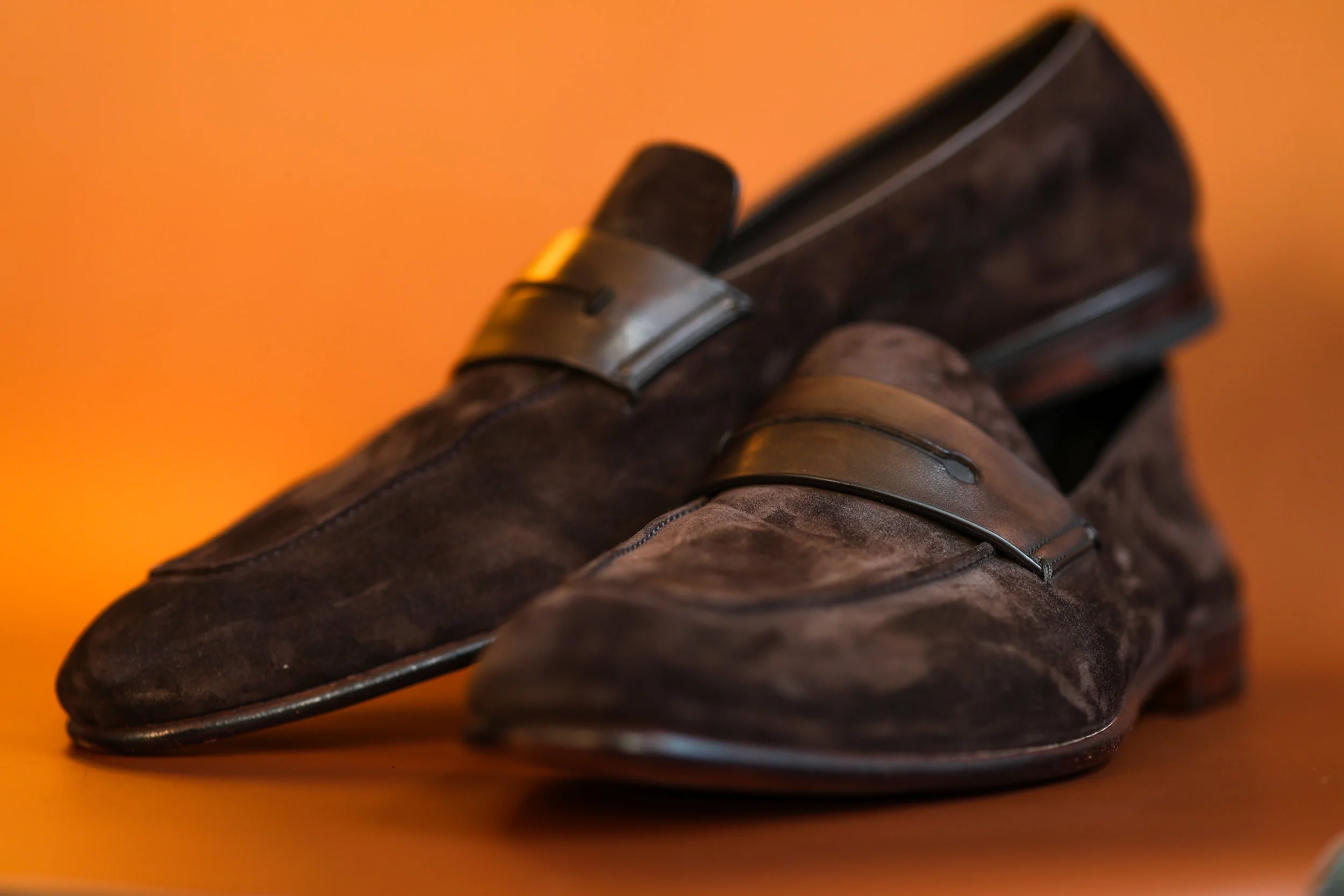 A pair of men's brown leather dress shoes with metal buckles, placed on an orange surface with an orange background.