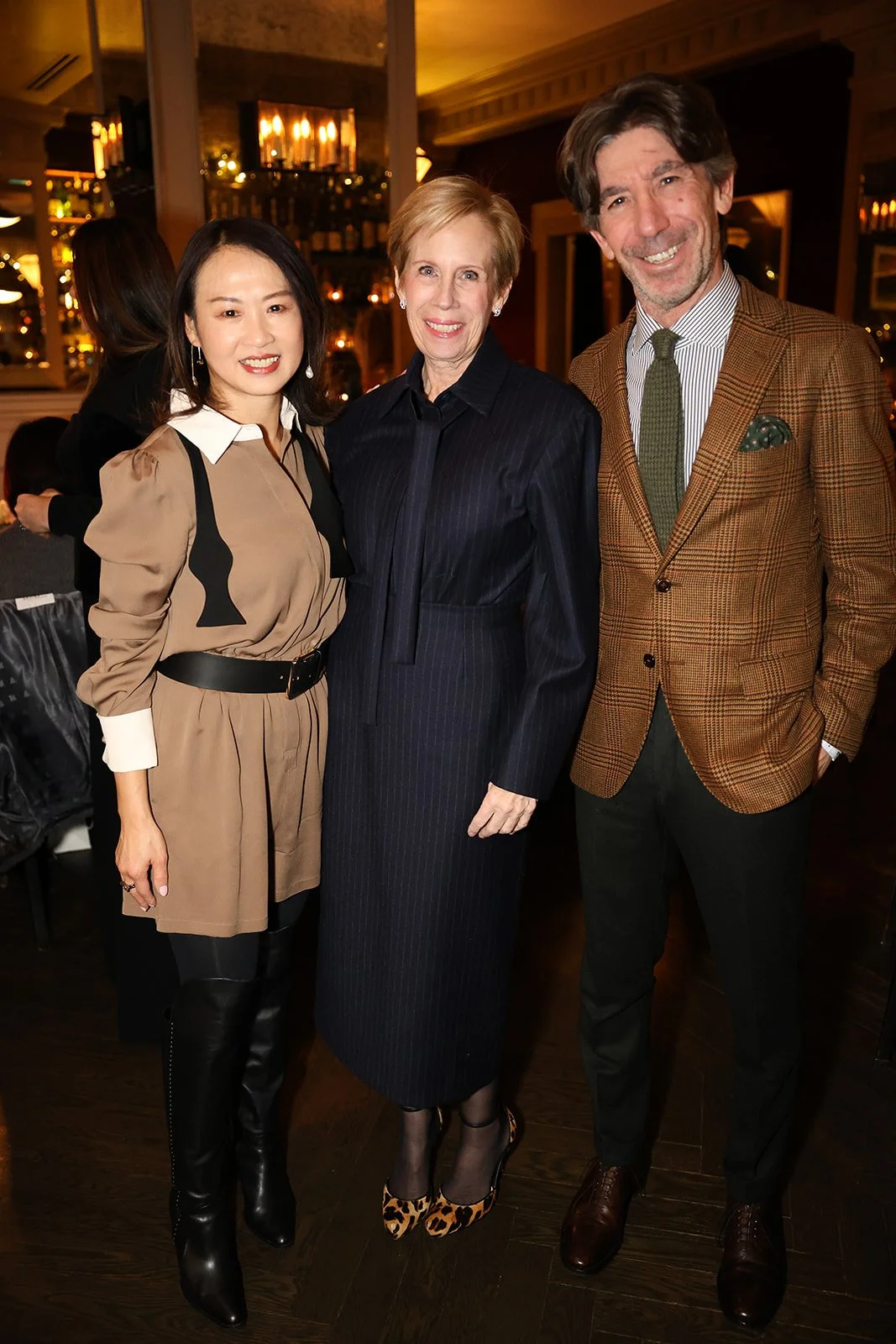 Three people posing together in an indoor setting, with warm lighting and a bar in the background.