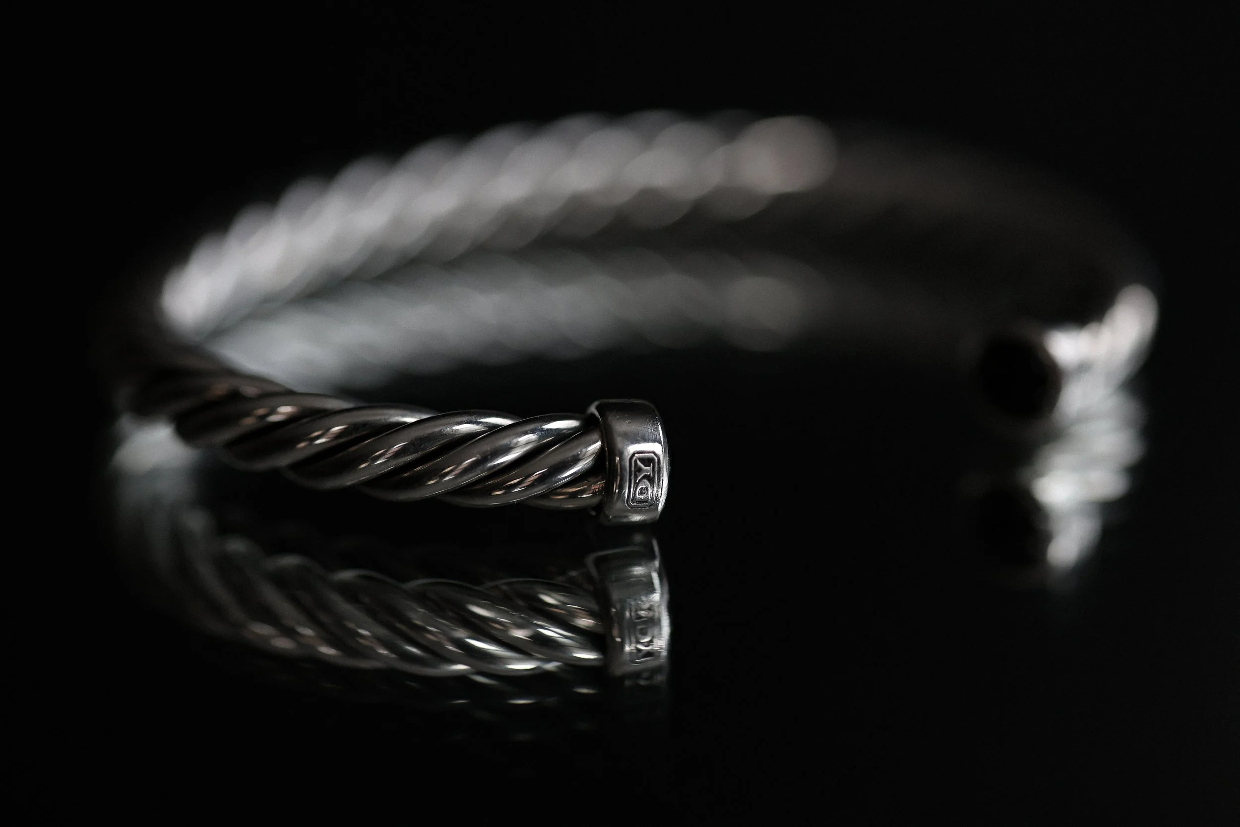 Close-up of a silver twisted metal bracelet on a black reflective surface.