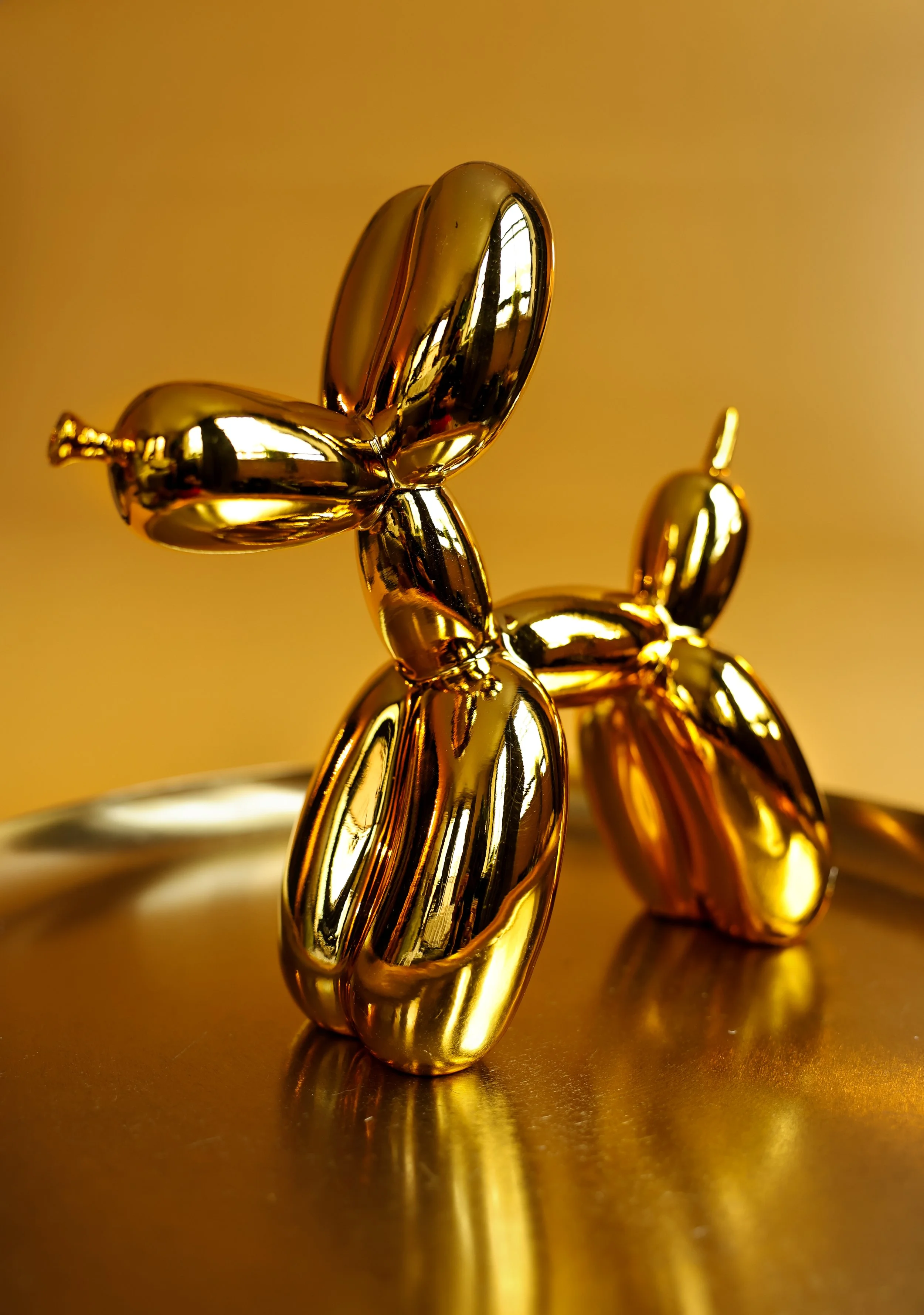 Close-up of a shiny, gold balloon animal sculpture resembling a dog, reflecting light and the surrounding environment.