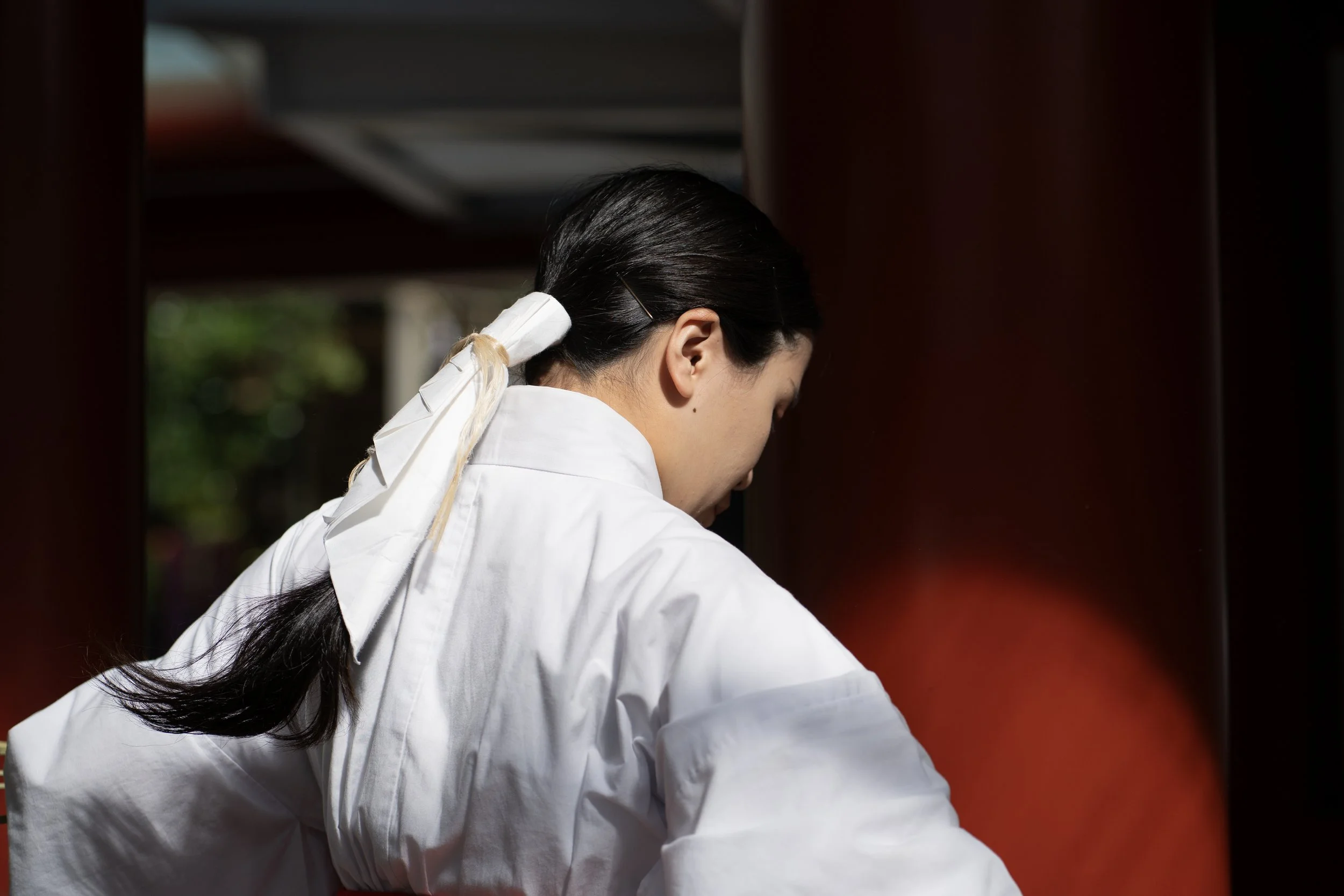A woman with long dark hair tied back, wearing a white coat, seen from behind, appears to be working or cleaning.