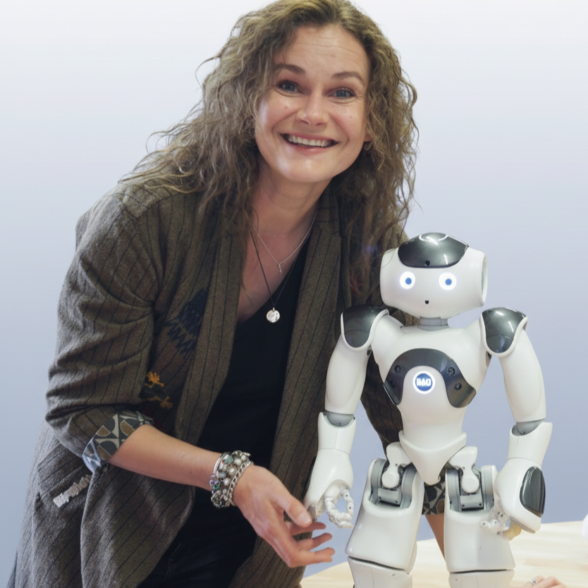 Inga Akulauskaite-Manocchia smiling next to a small white humanoid Nao robot on a table.